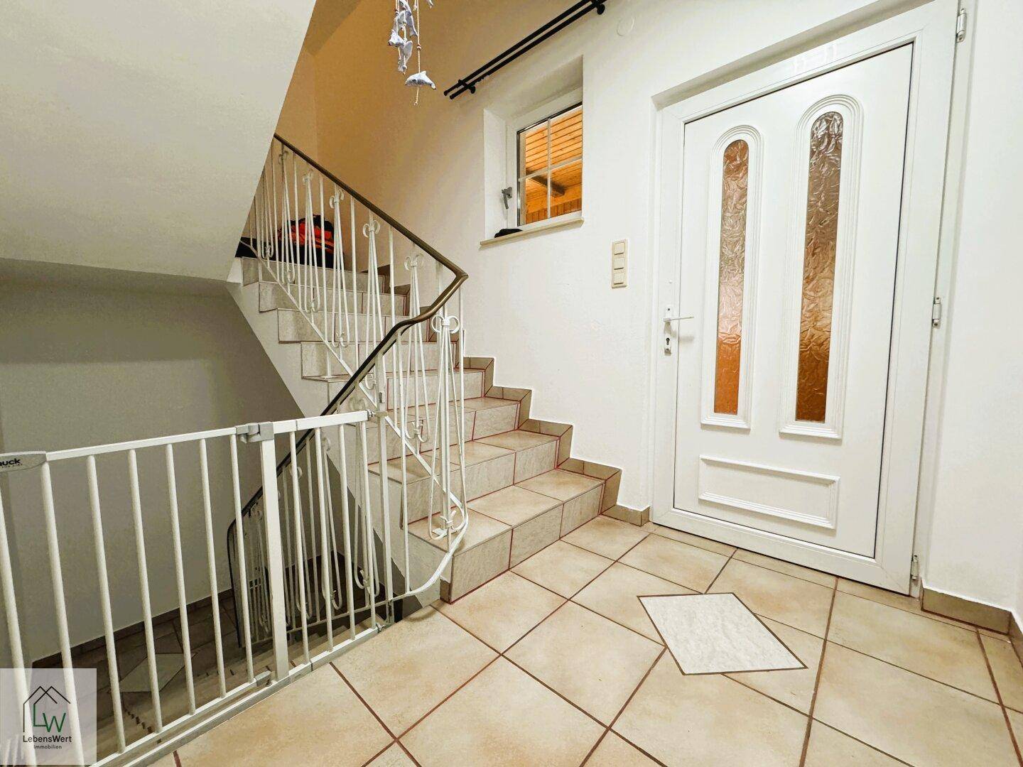 Eingangsbereich mit gefliestem Boden, Treppe ins Obergeschoss und heller Haustür.