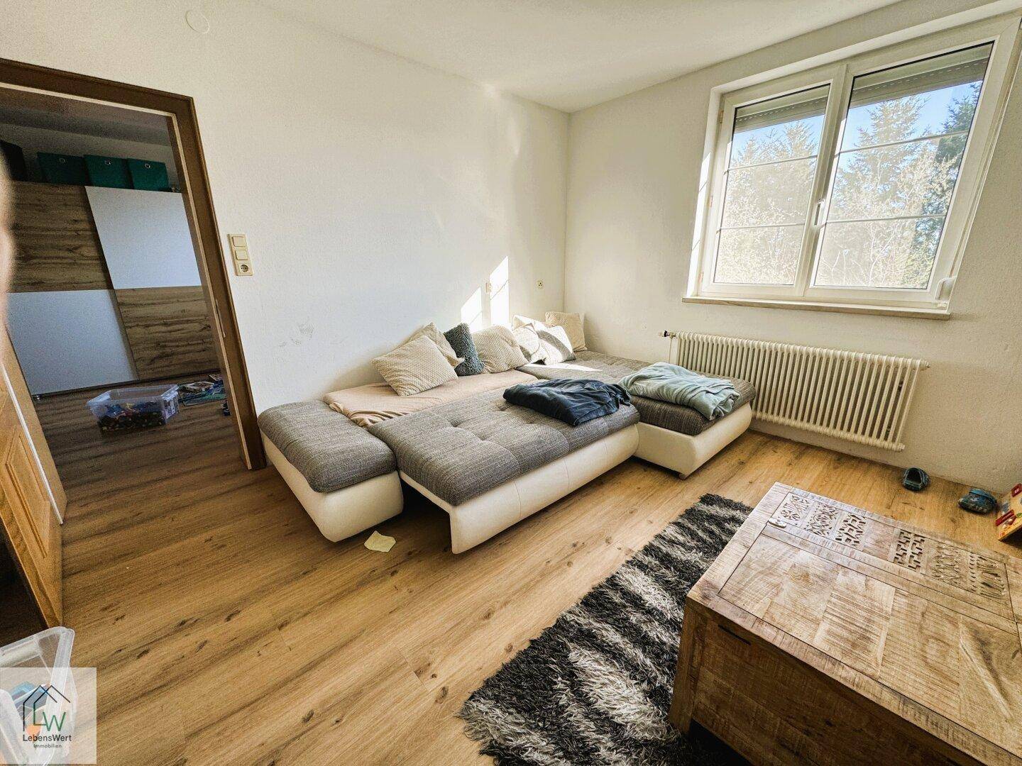 Helles Wohnzimmer mit bequemer Couch, Holztisch und Laminatboden.