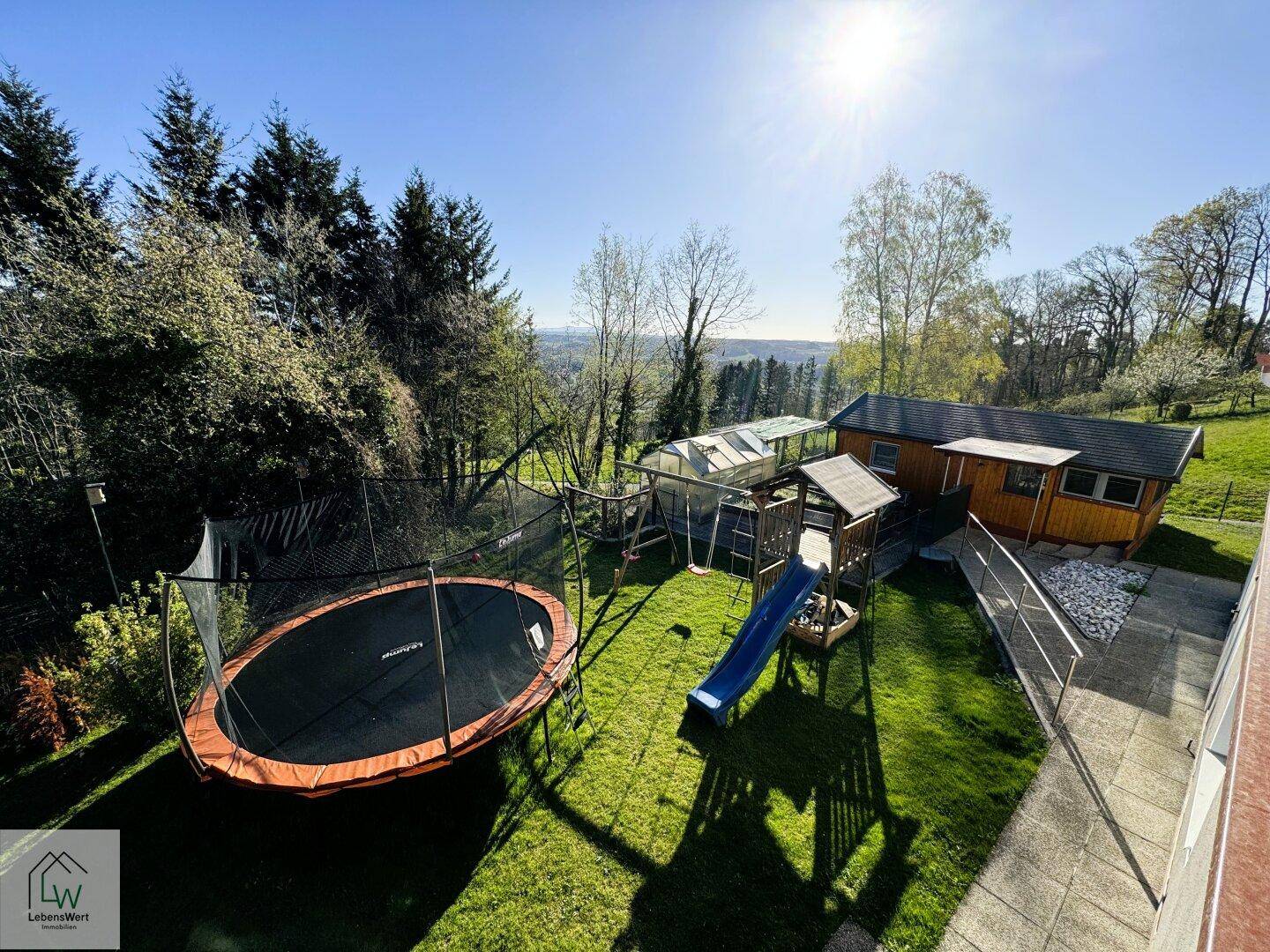 Weitläufiger Garten mit Trampolin, Spielplatz und Blick auf die umliegende Landschaft.