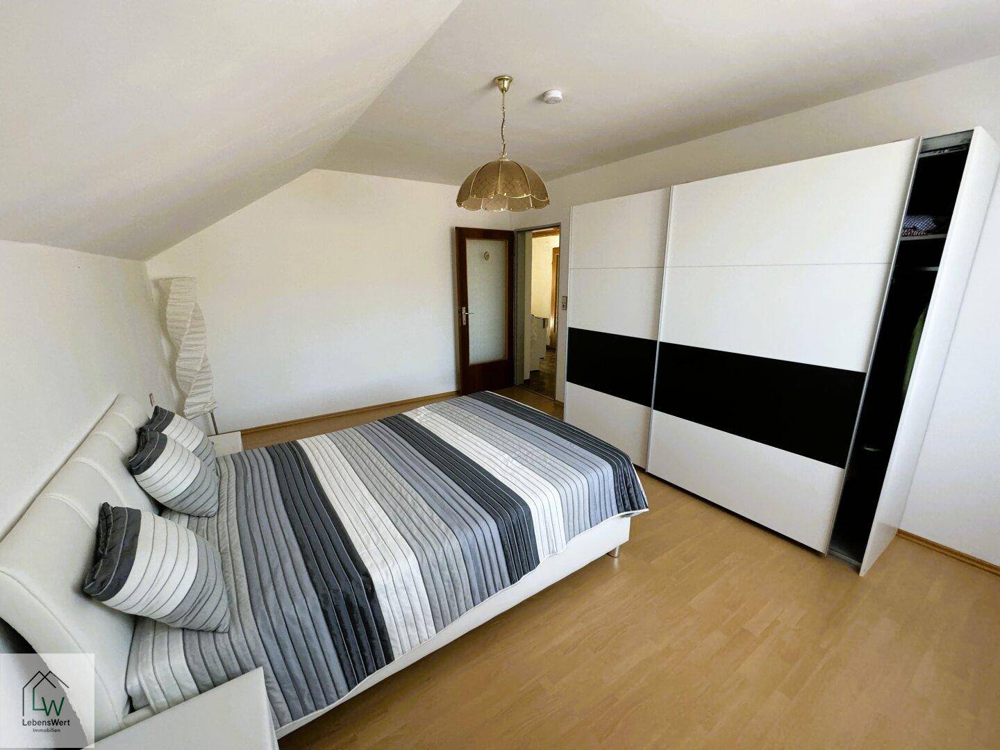 Schlafzimmer mit Doppelbett, großem Schiebeschrank und Laminatboden unter Dachschräge.