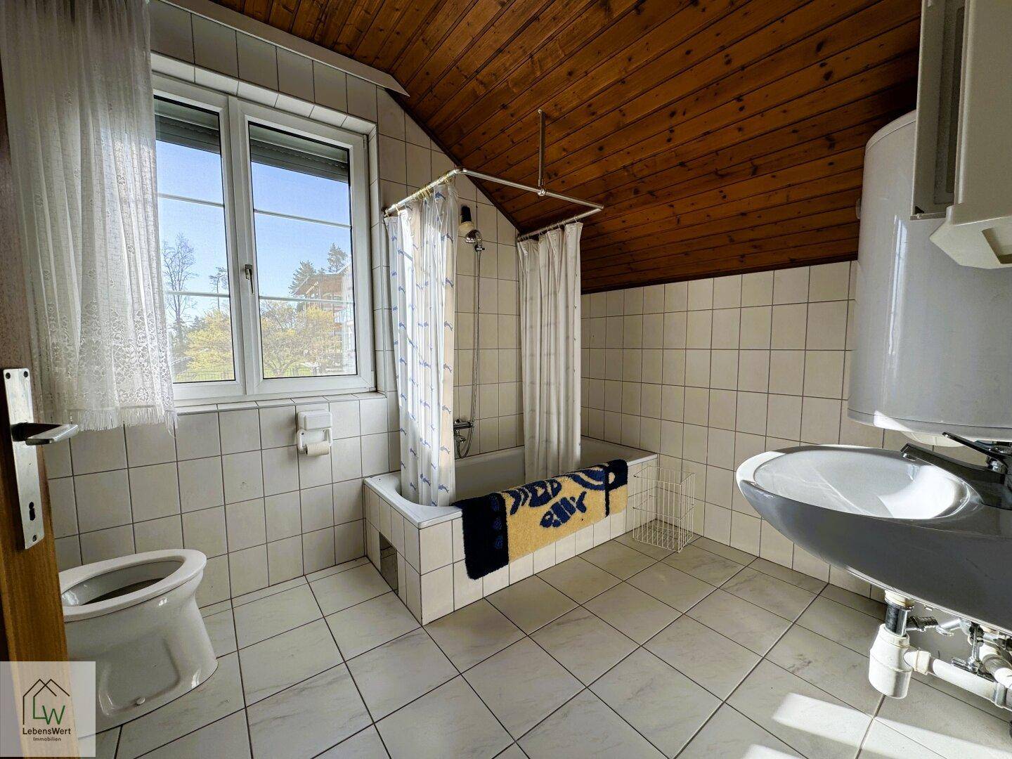Badezimmer im Dachgeschoss mit Badewanne, WC, Waschbecken und Holzdecke.