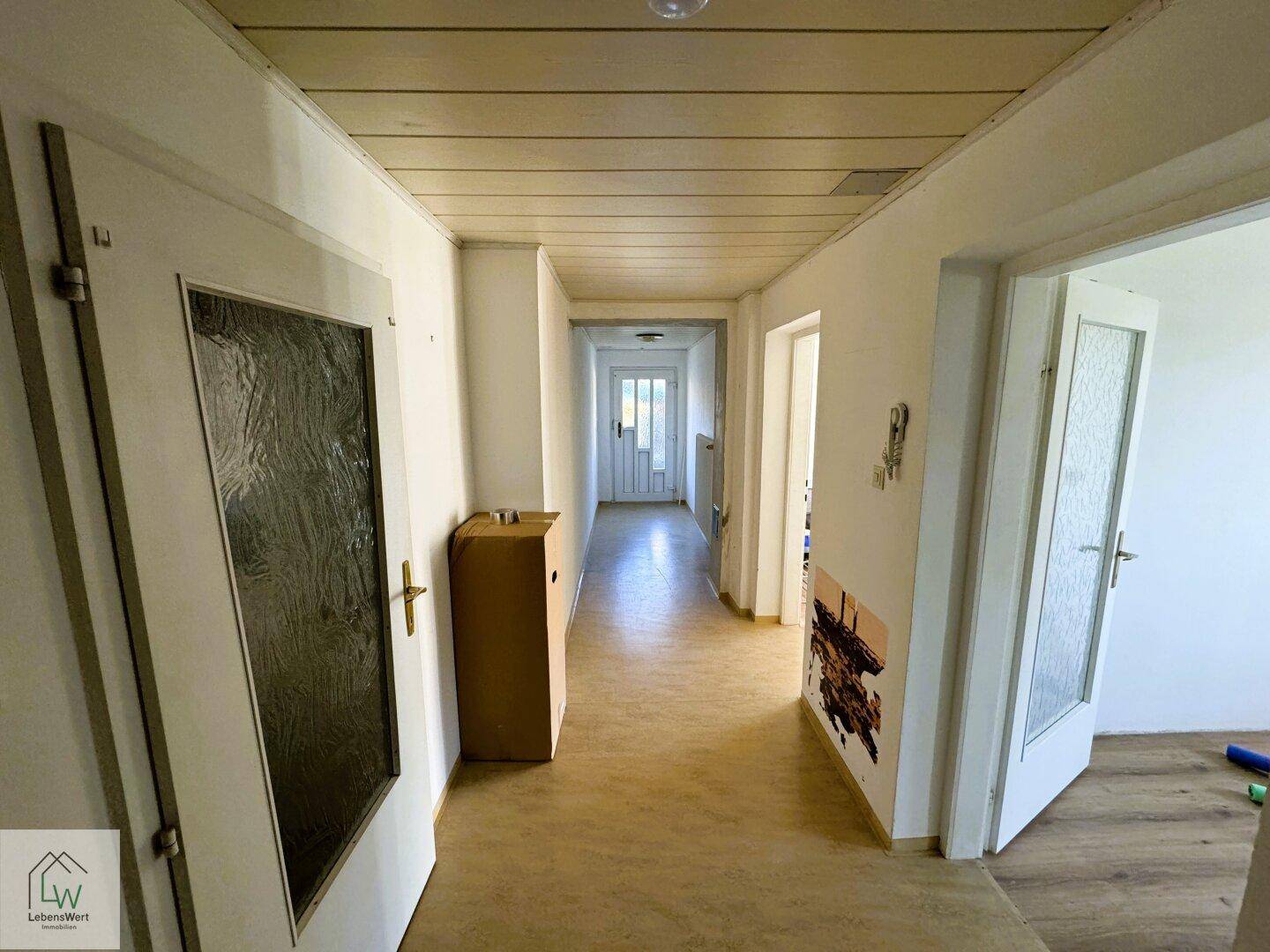 Heller Flur mit Holzdeckenverkleidung und Laminatboden, der zu weiteren Räumen führt.