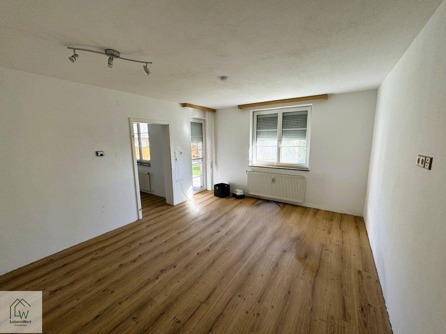 Leerer Raum mit Laminatboden, weißen Wänden und Fenster, bereit zur individuellen Gestaltung.