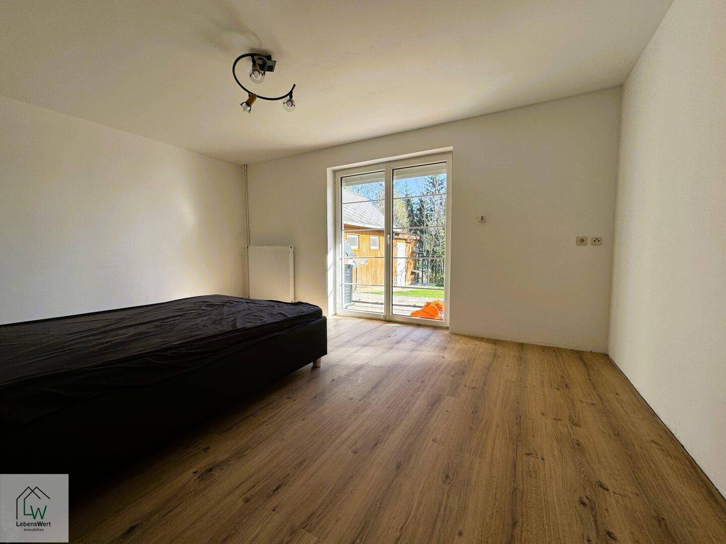 Helles Schlafzimmer mit Laminatboden und großer Glastür zum Außenbereich.