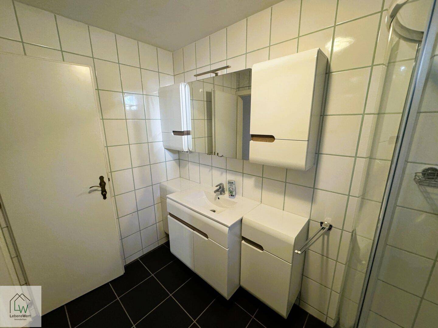 Badezimmer mit weißem Waschtisch, Spiegelschrank und Duschkabine.