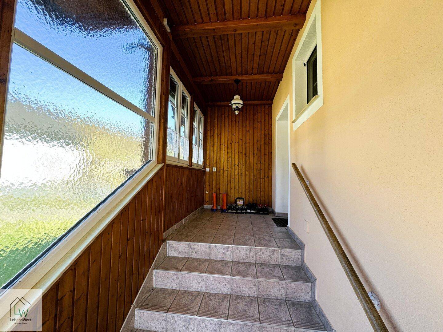 Geräumiger Flur mit Holzdecke, großen Fenstern und Treppe zum oberen Bereich.