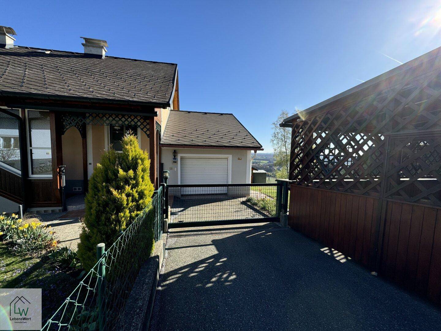 Außenansicht des Hauses mit Einfahrt, Garage und Carport unter blauem Himmel.