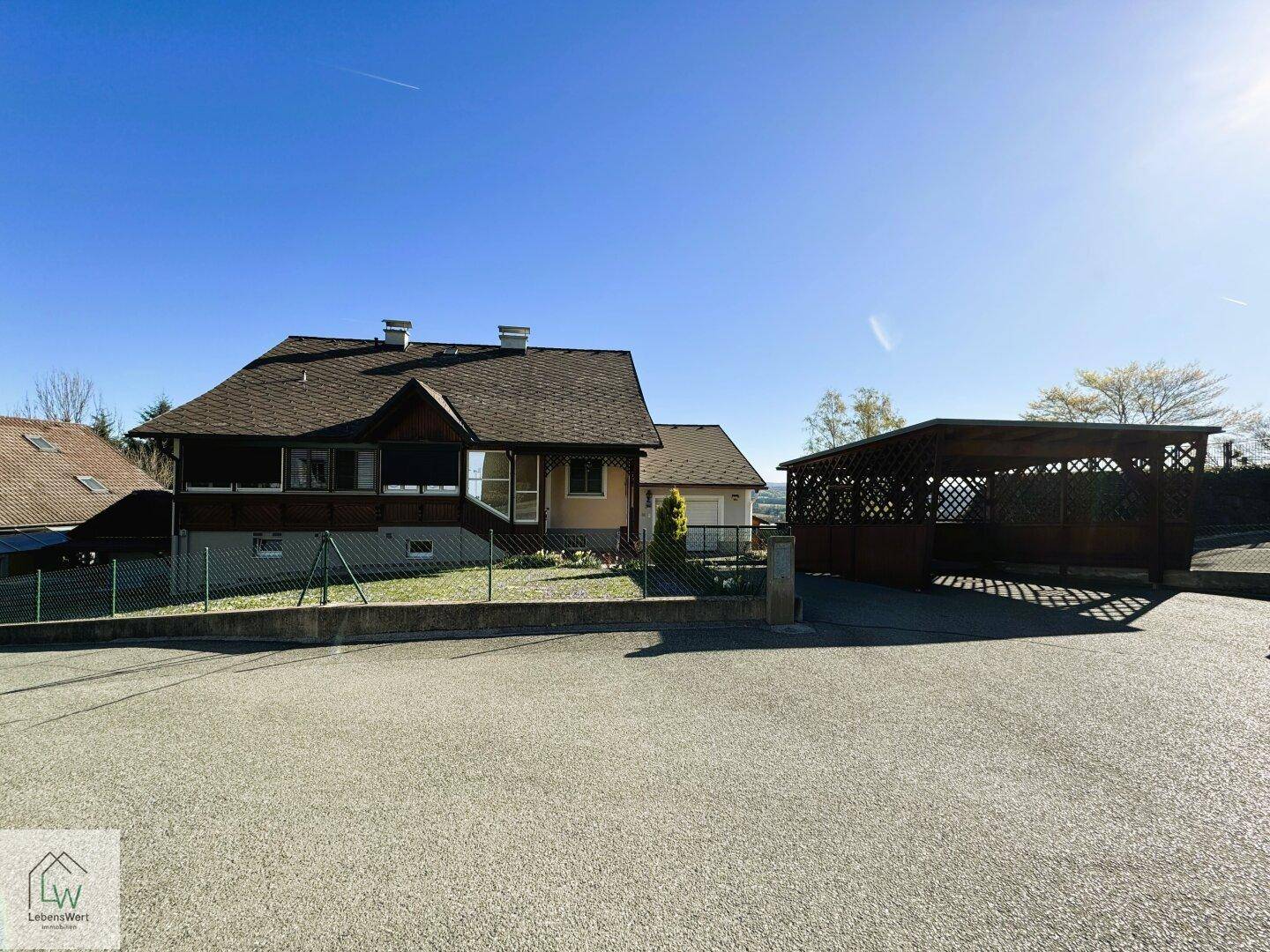 Gesamtansicht des Einfamilienhauses mit Carport und weitläufiger Einfahrt an einem sonnigen Tag.