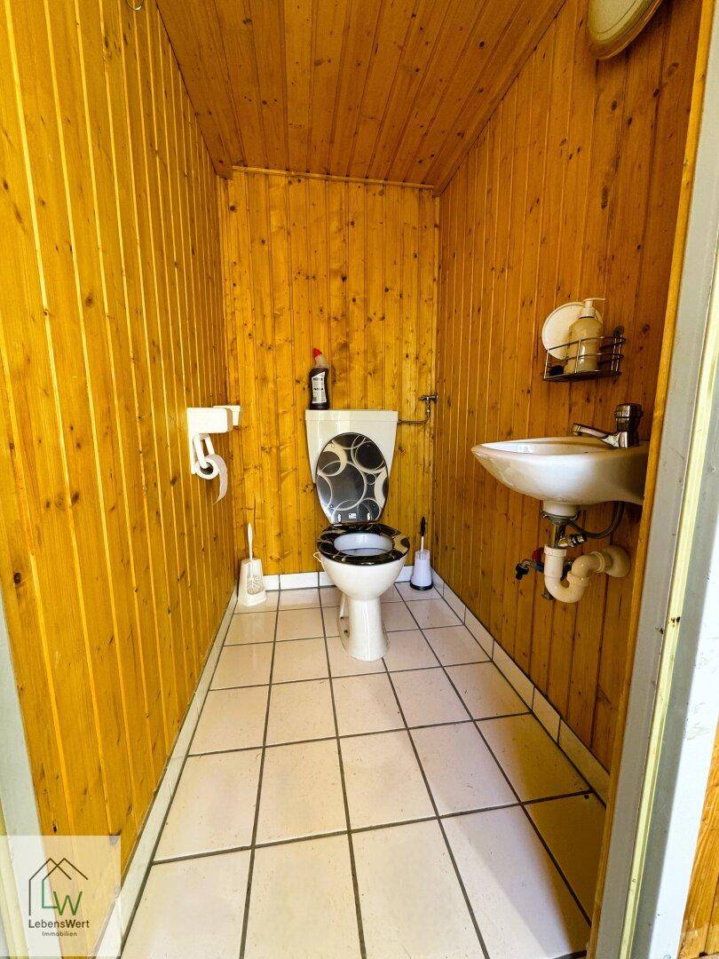 Kleines WC im Gartenhaus mit Holzverkleidung und gefliestem Boden.