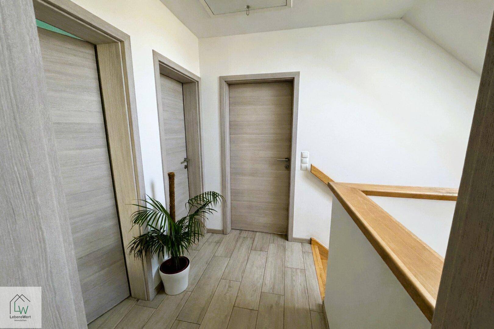Heller Flur im Obergeschoss mit Holztüren und Fliesenboden, der zu den Zimmern führt.