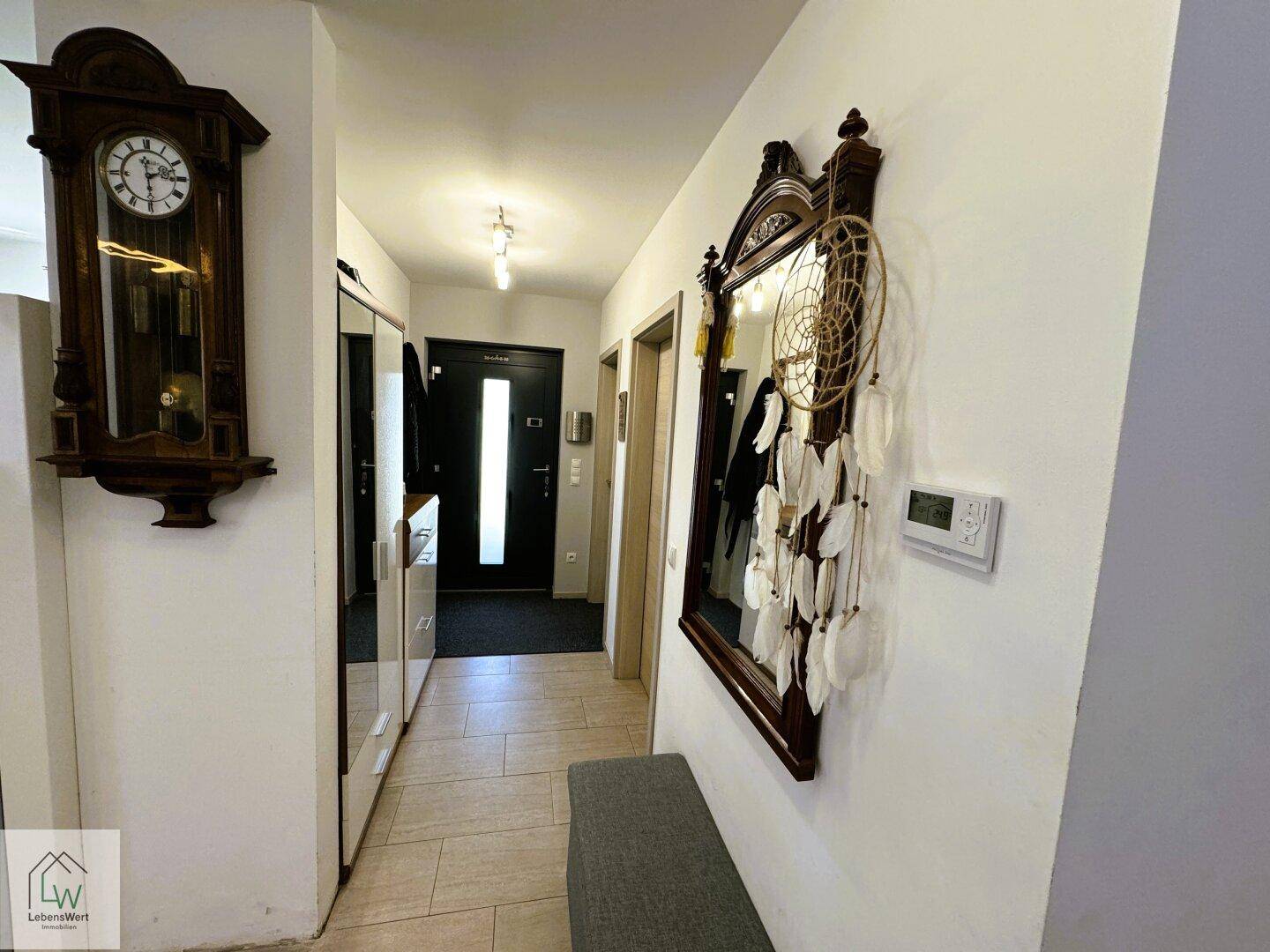 Geräumiger Flur mit Fliesenboden, Spiegel und traditioneller Wanduhr.