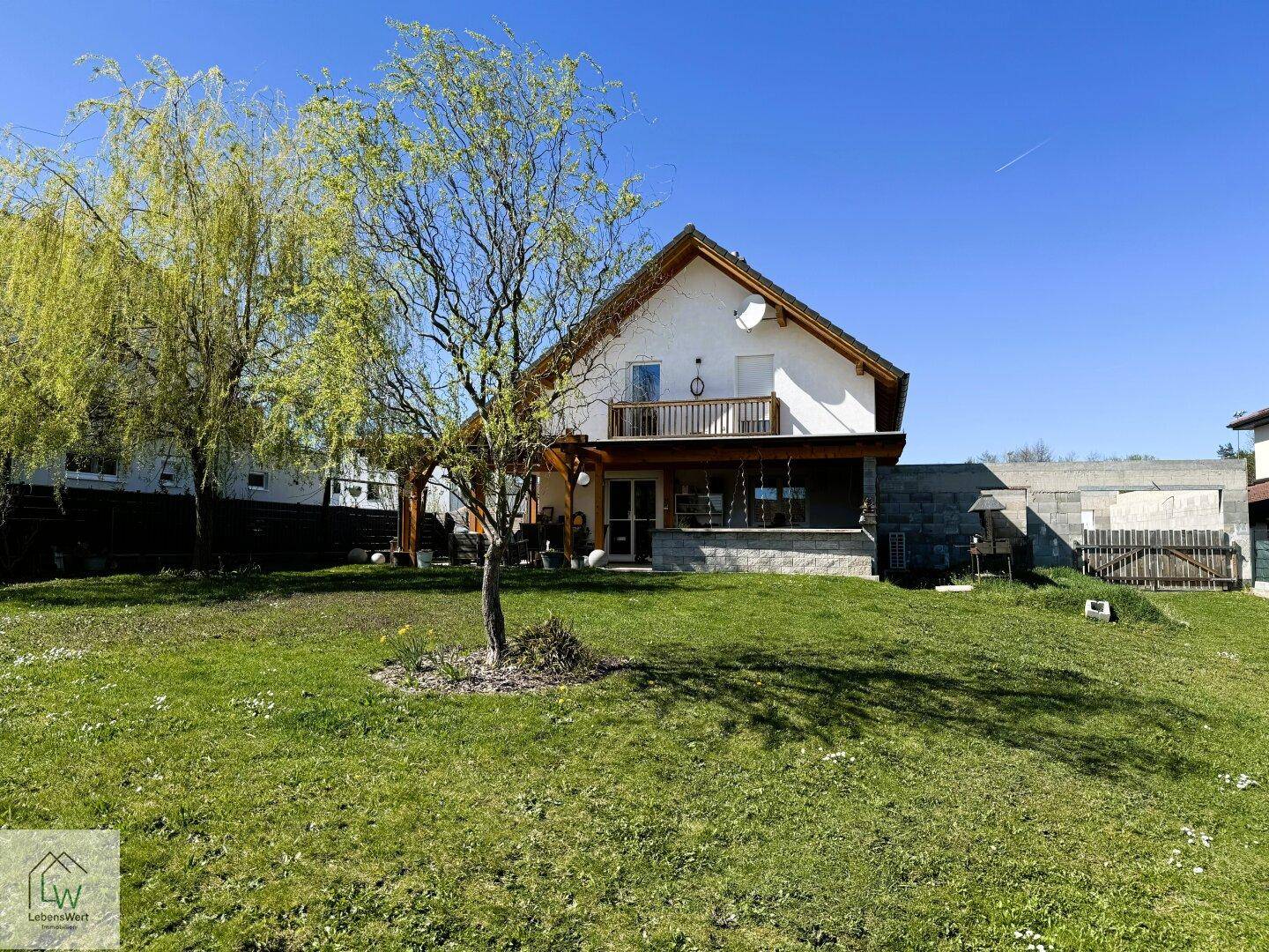 Weitläufiger Garten mit Rasenfläche und blühenden Bäumen, Blick auf das Haus.