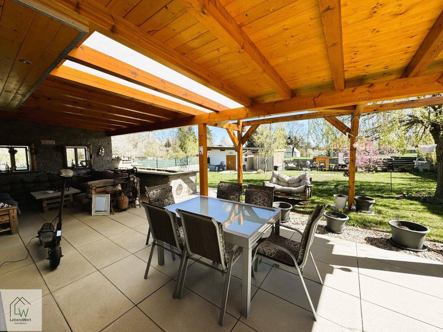Überdachte Terrasse mit großem Esstisch und Blick auf den Garten, ideal für Mahlzeiten im Freien.
