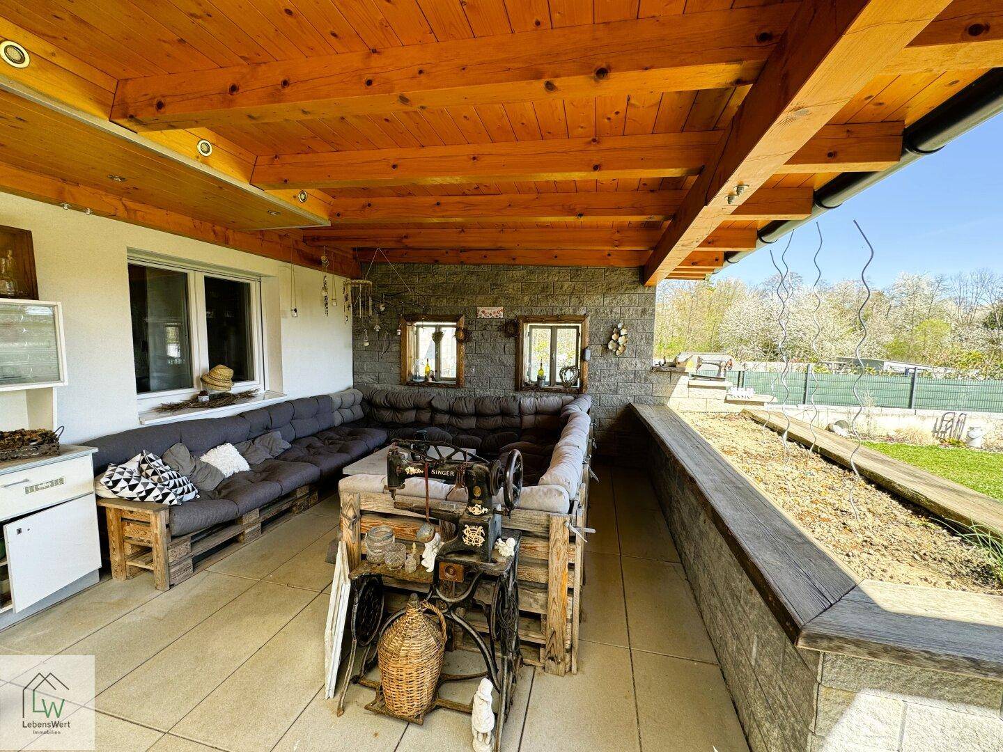 Gemütlicher Lounge-Bereich auf der überdachten Terrasse mit Palettenmöbeln und Steinwand.