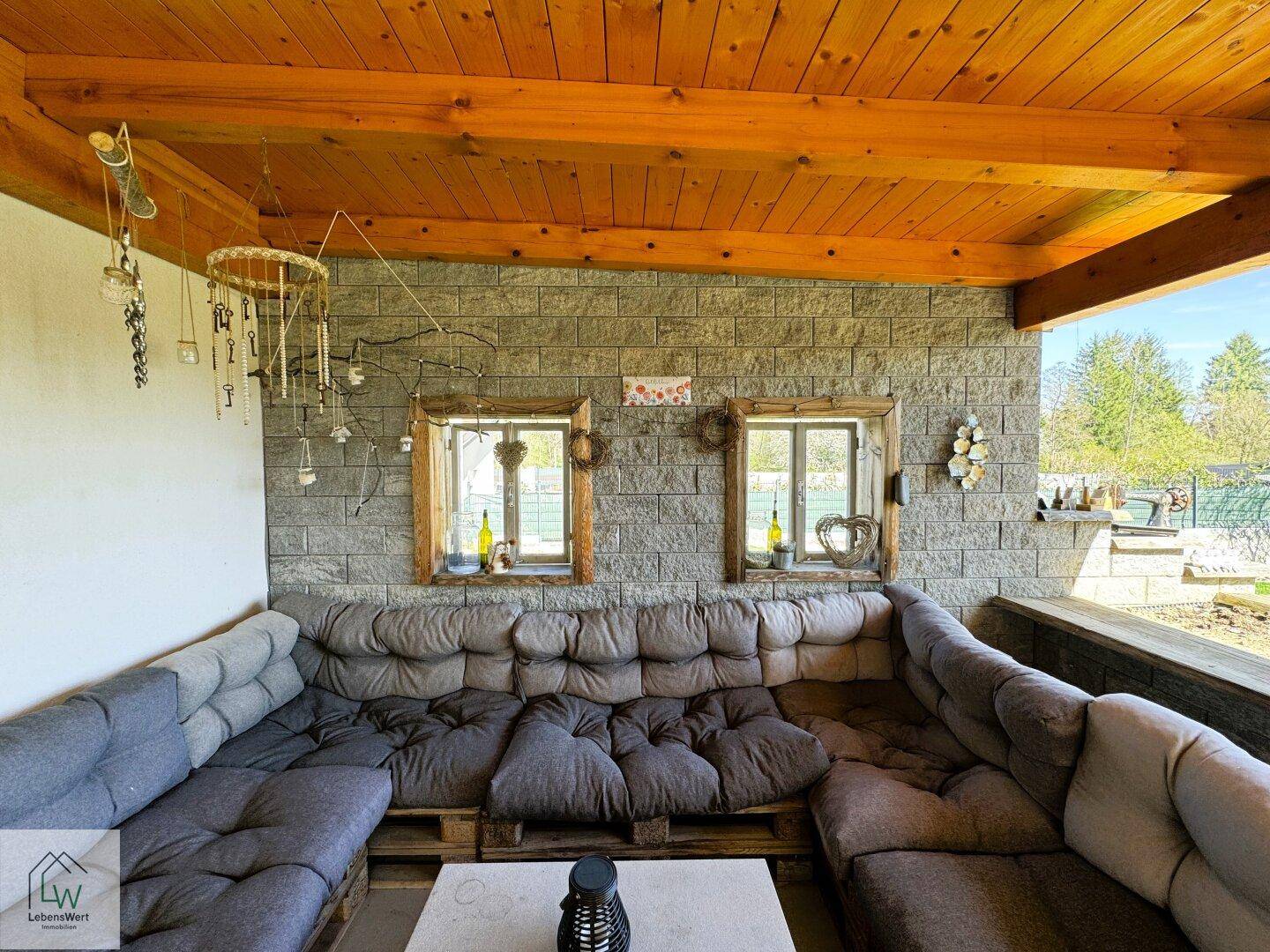 Überdachter Lounge-Bereich auf der Terrasse mit Steinwand und gemütlichen Sitzgelegenheiten.