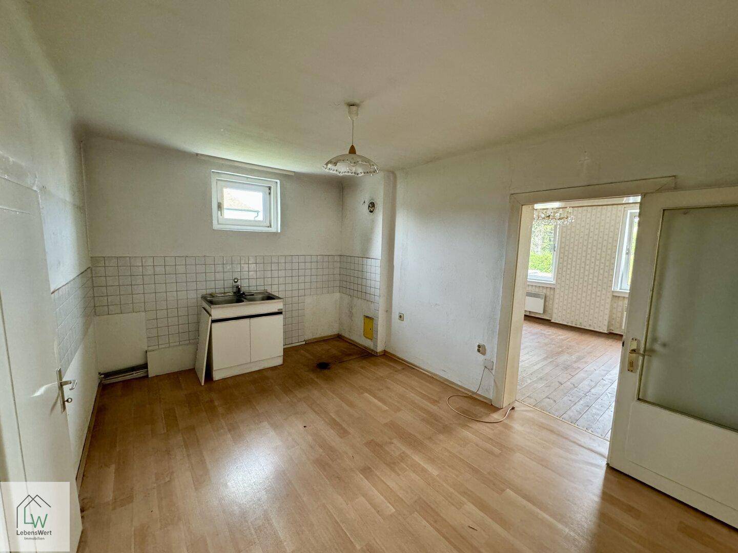 Einfache Küche mit Spülbecken, Fliesenwand und Laminatboden, bereit zur Renovierung.