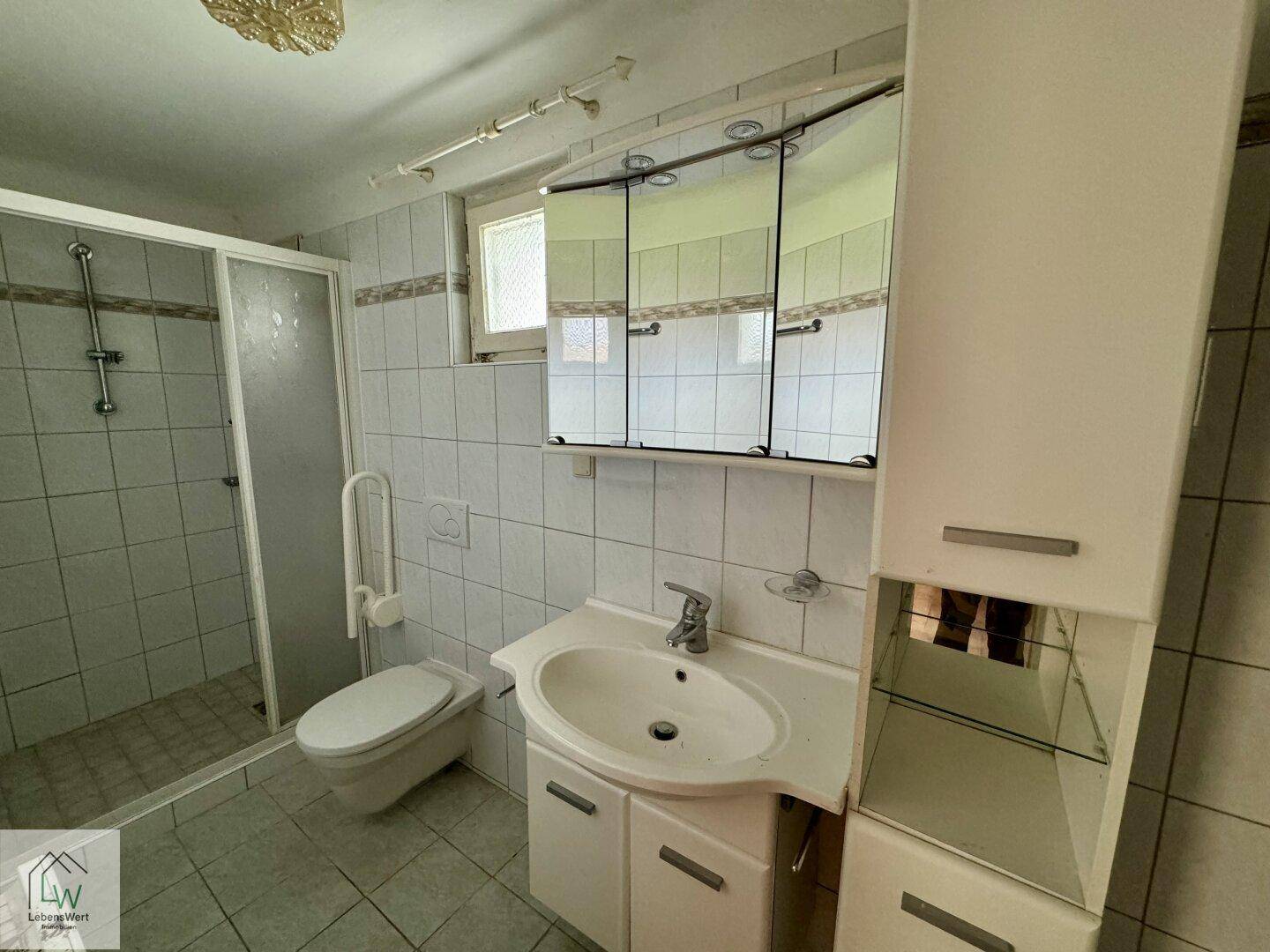 Badezimmer mit Dusche, WC, Waschbecken und Spiegelschrank, in älterem Zustand.