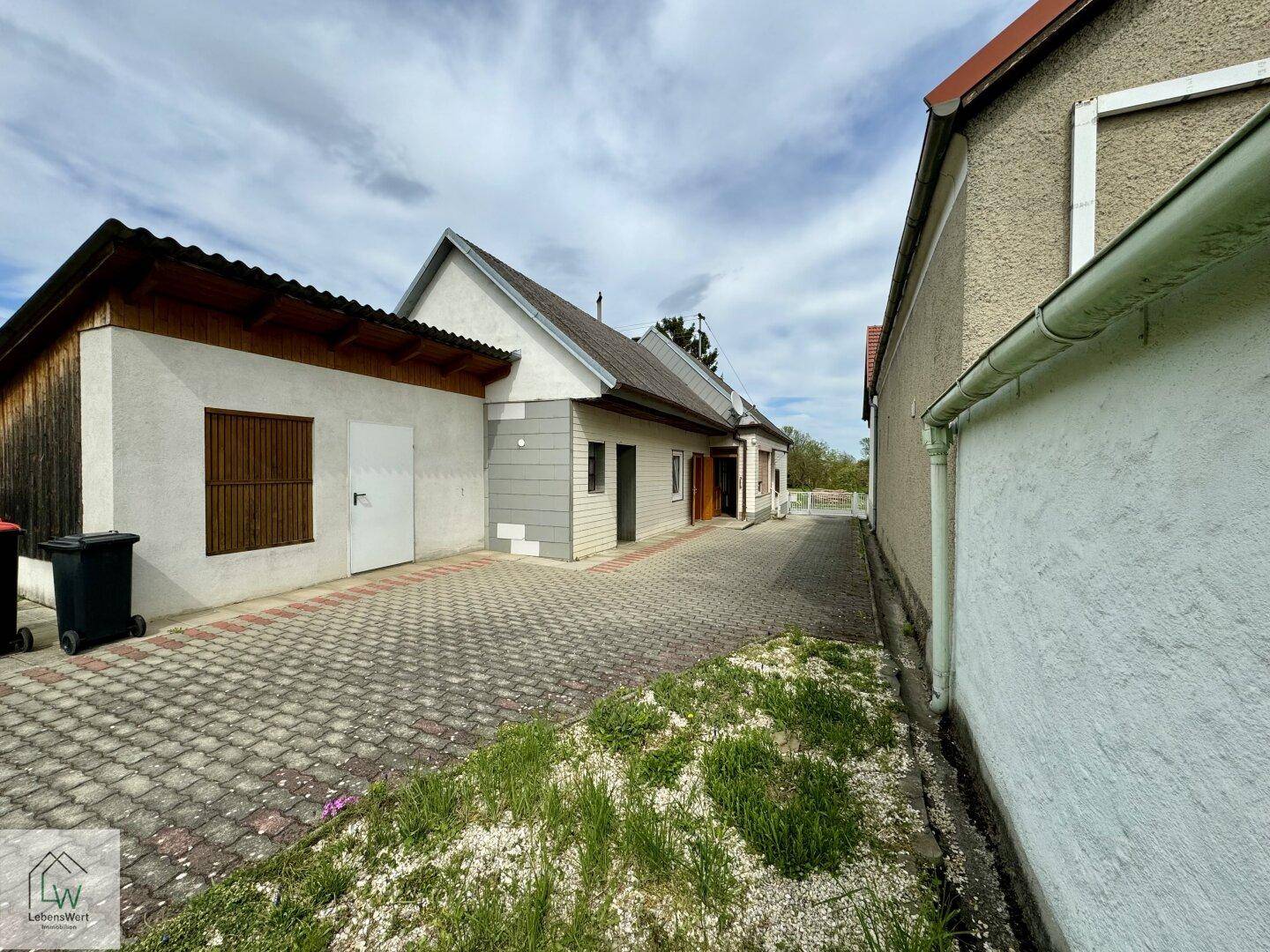 Gepflasterter Hofbereich zwischen mehreren Gebäuden mit Mülltonnen und Zugangstüren.