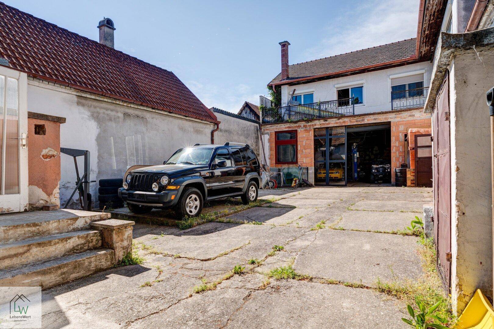 Geräumiger Innenhof mit einem geparkten Auto und mehreren Gebäuden unter blauem Himmel.