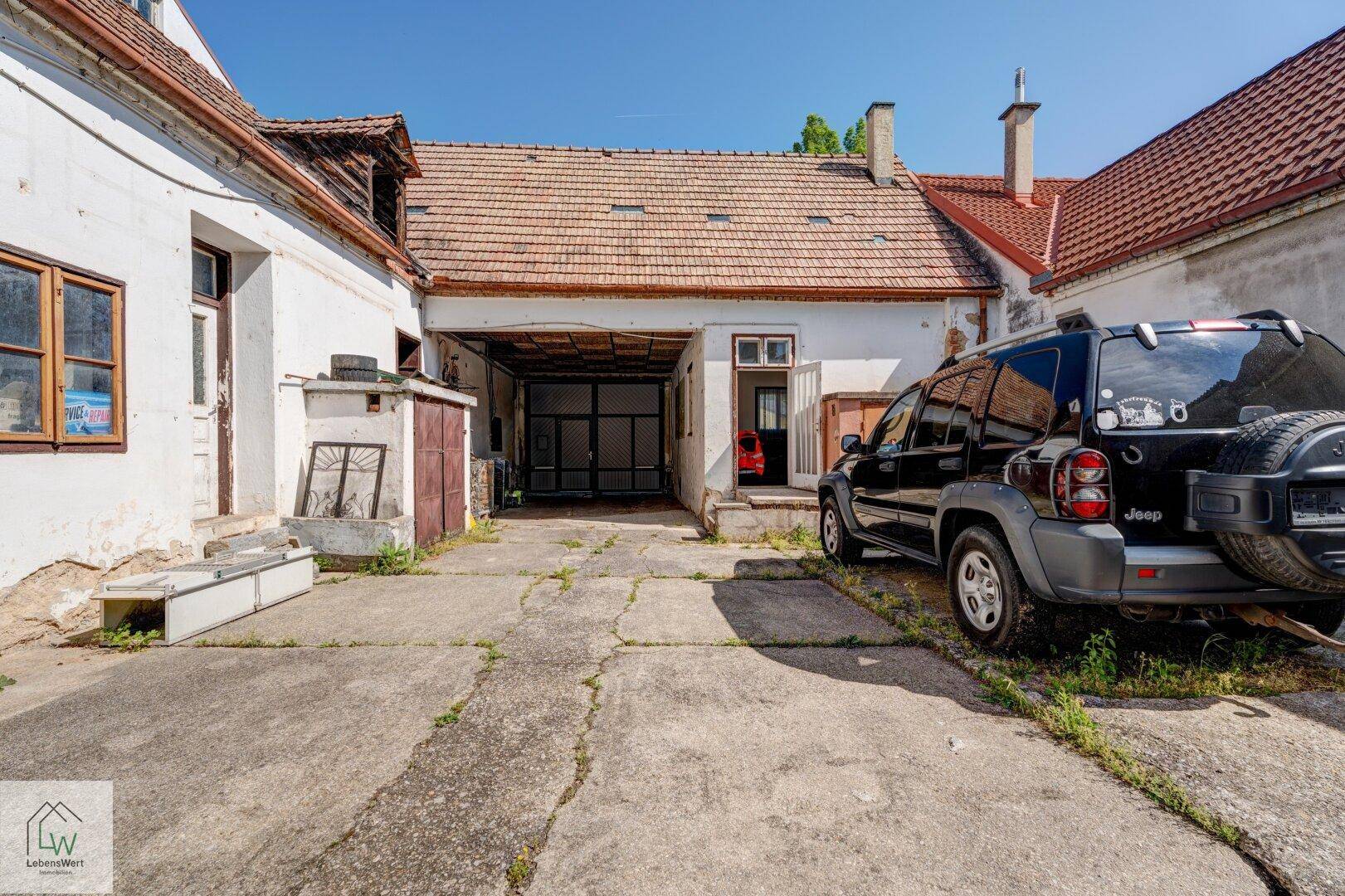 Weiterer Blick auf den Innenhof mit einem geparkten Geländewagen und verschiedenen Nebengebäuden.