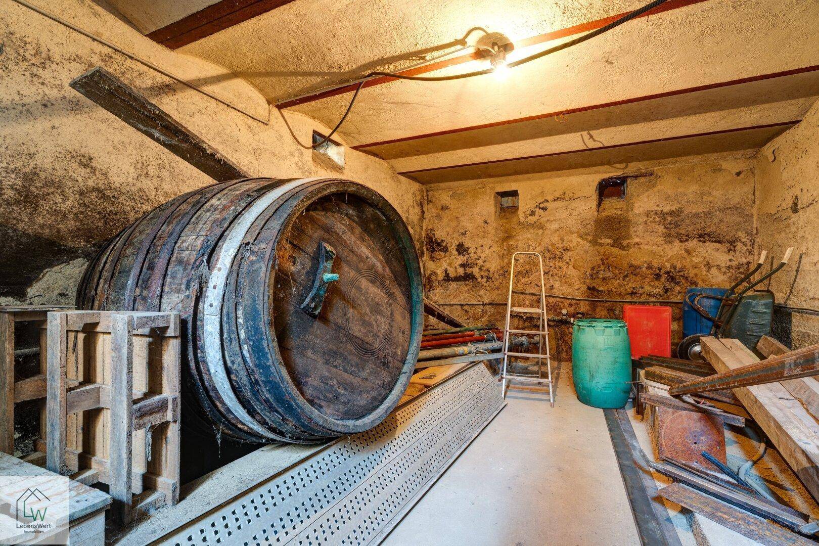 Rustikaler Kellerraum mit einem großen Holzfass und verschiedenen Lagergegenständen.