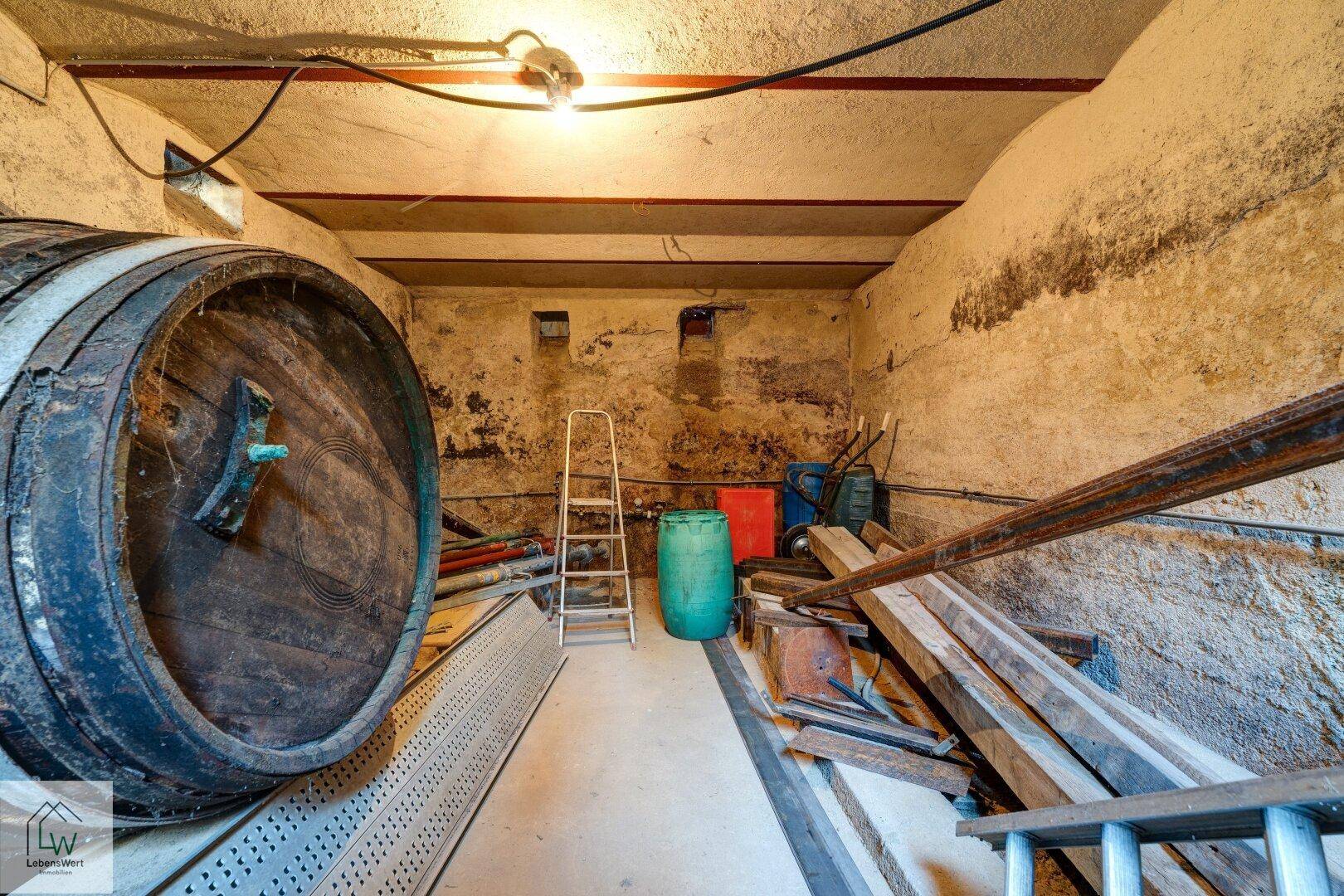 Geräumiger Keller mit einem imposanten Holzfass und Lagerflächen für diverse Materialien.