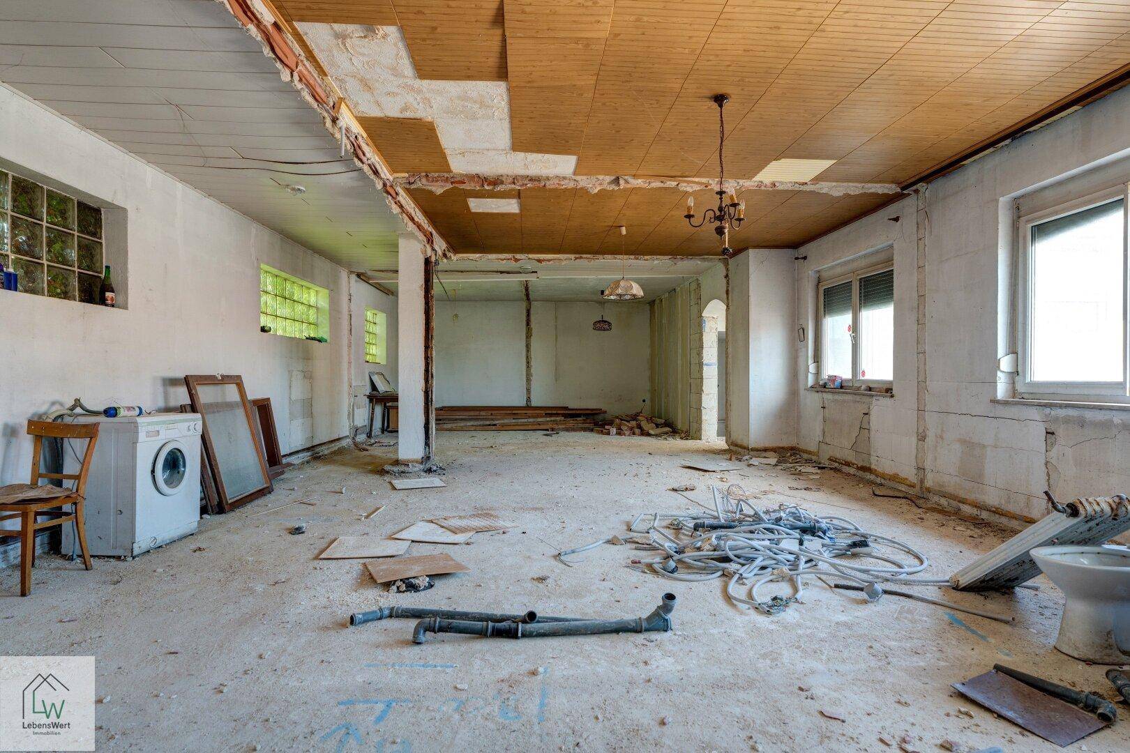 Renovierungsbedürftiger Raum mit freigelegten Wänden, Deckenverkleidung und Baumaterialien.
