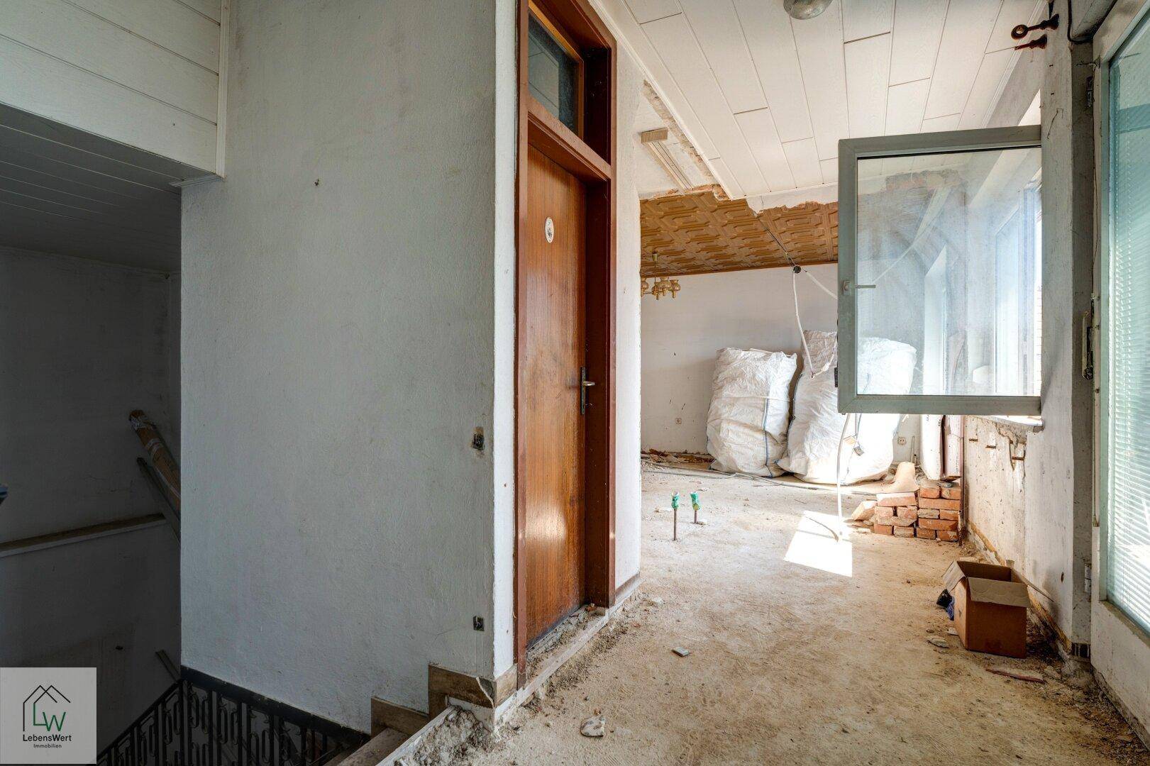 Treppenhaus mit Blick in einen angrenzenden Raum, der sich im Renovierungszustand befindet.
