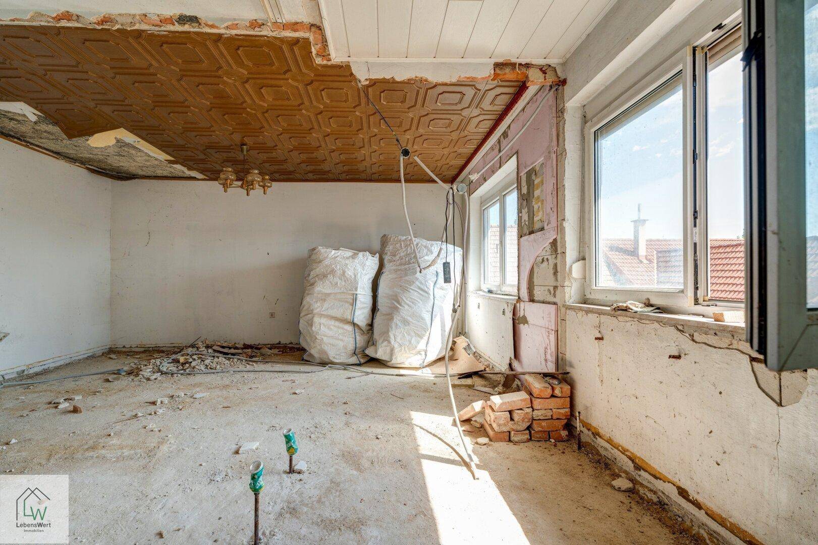 Renovierungsbedürftiger Raum mit großen Fenstern, dekorativer Decke und Baumaterialien.