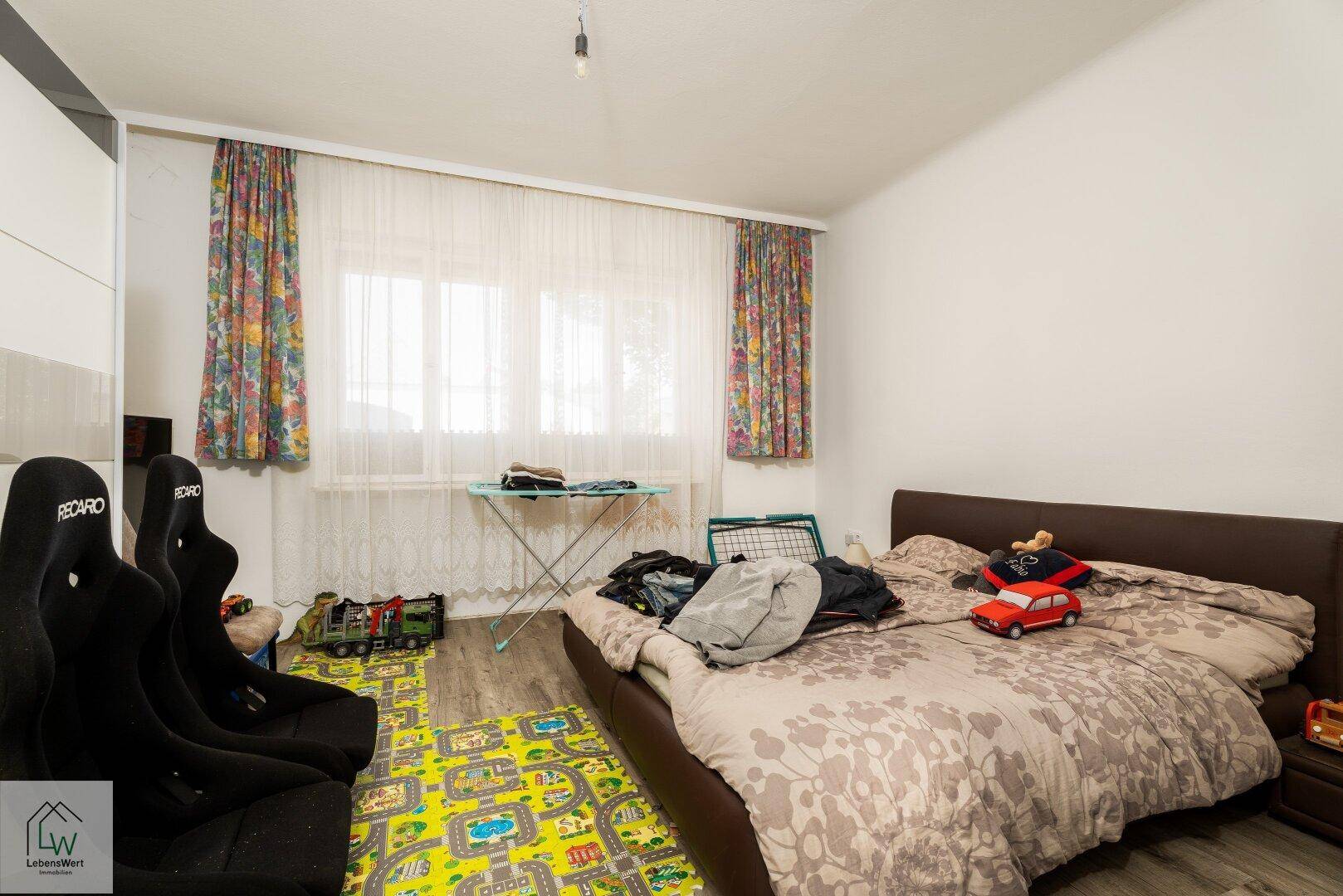Schlafzimmer mit Doppelbett, Holzboden und bunten Vorhängen, eingerichtet für Kinder.