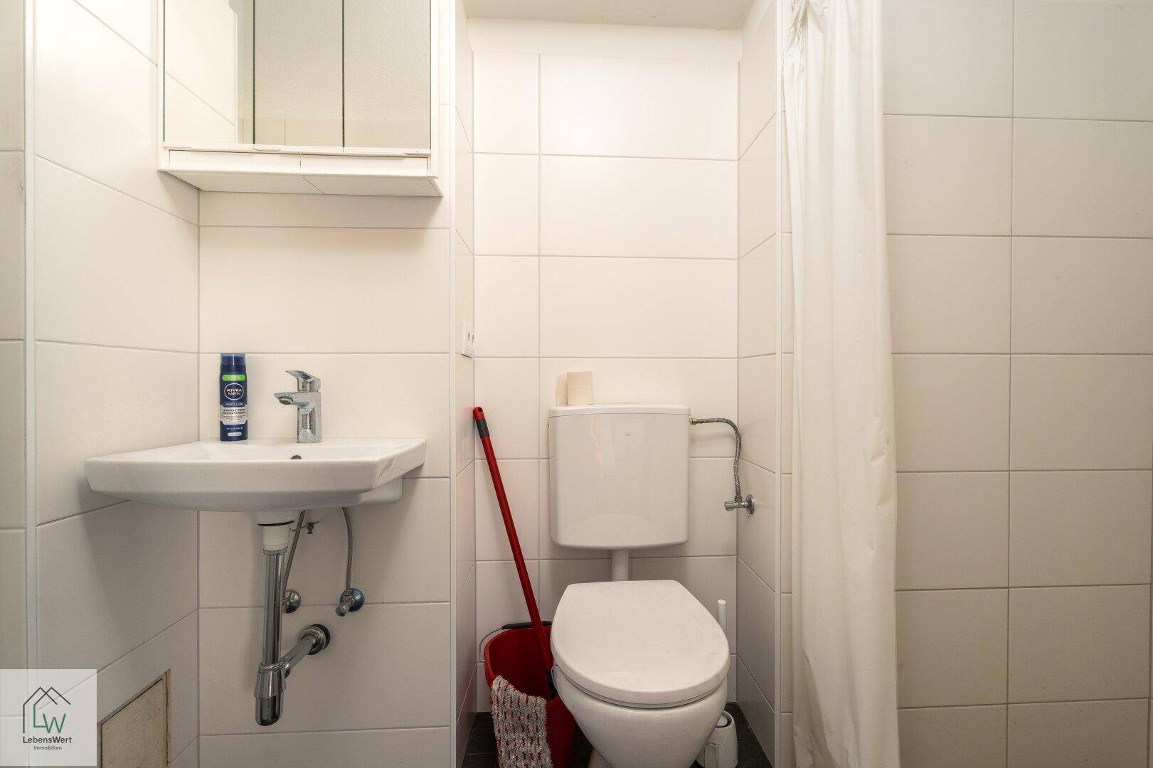 Kleines Badezimmer mit WC, Waschbecken und Duschvorhang, komplett gefliest in Weiß.