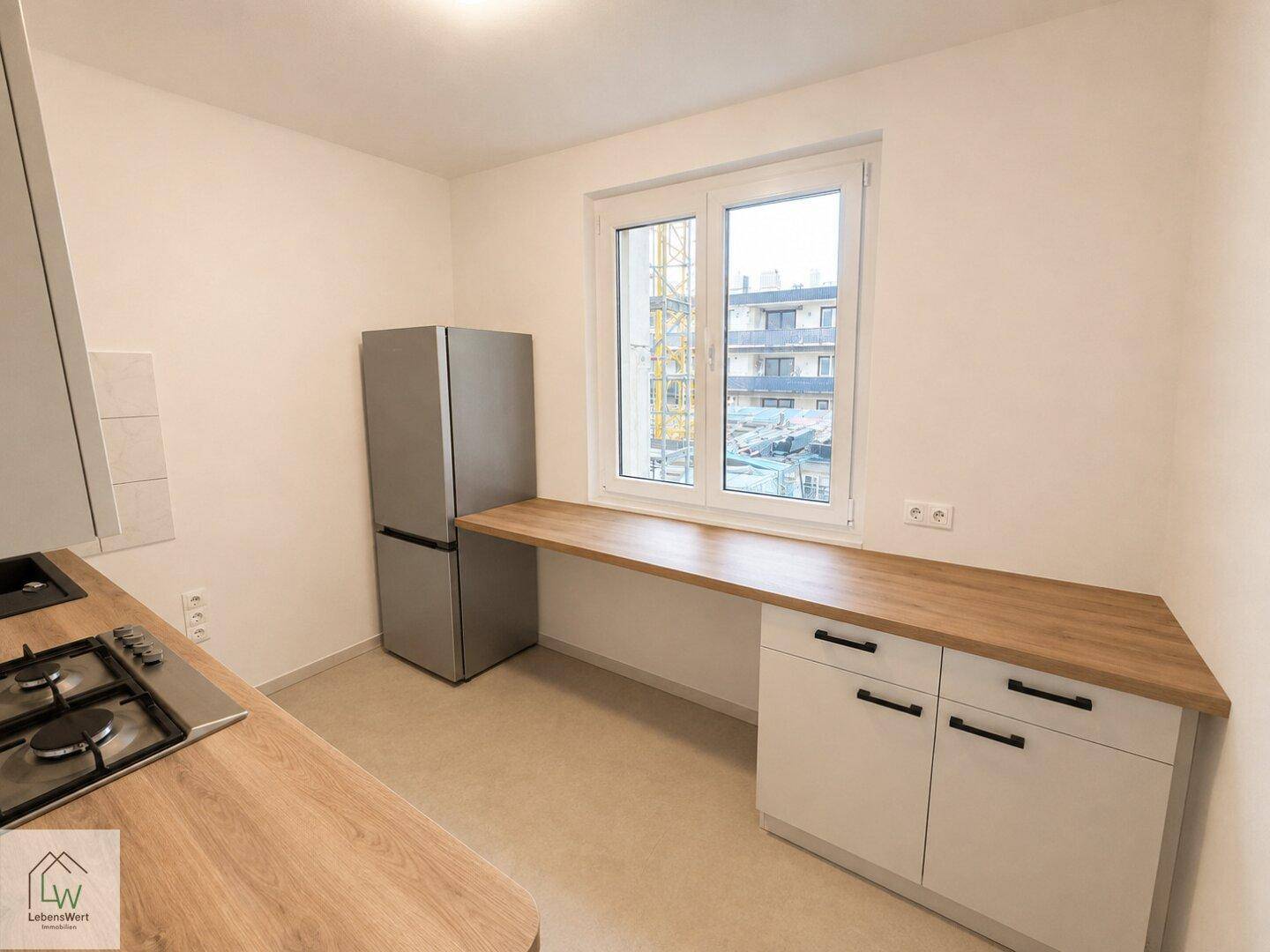Helle Küche mit Fenster, erweitertem Arbeitsbereich und Kühlschrank.