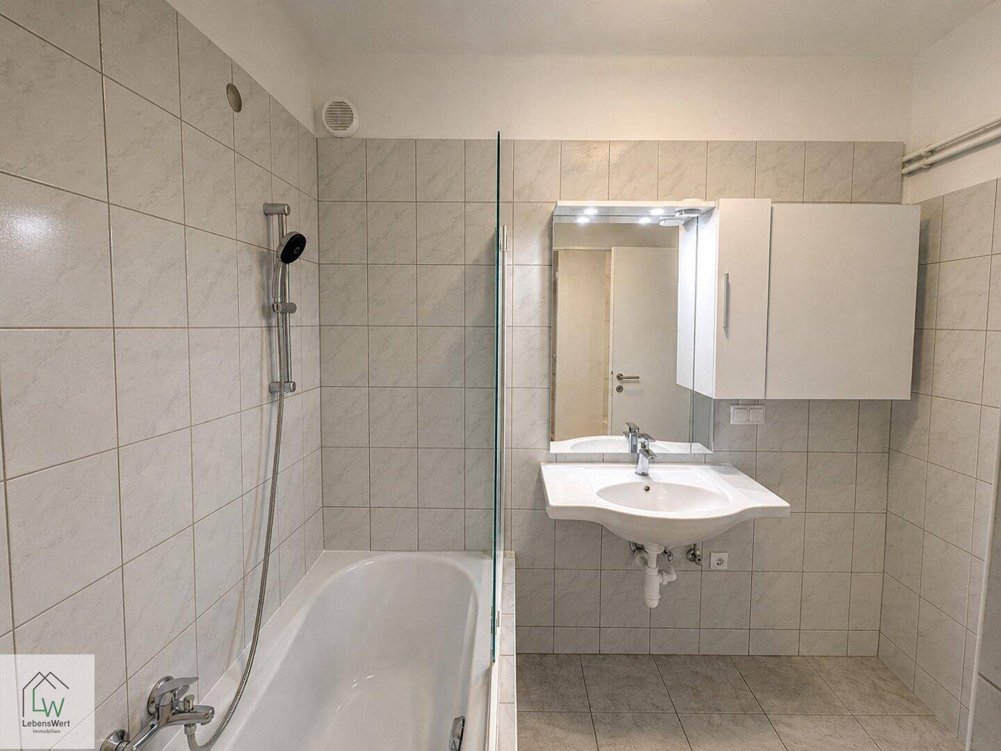 Helles Badezimmer mit Badewanne, Duschfunktion, Waschbecken und Spiegelschrank.