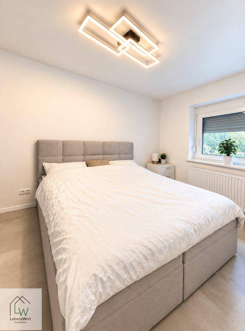 Helles Schlafzimmer mit großem Doppelbett, modernem Deckenlicht und Fenster.