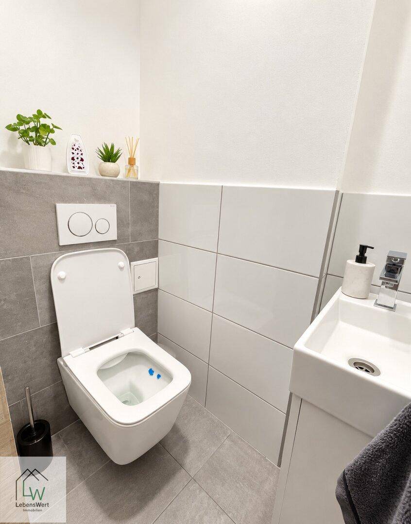 Modernes Gäste-WC mit Wand-WC, kleinem Waschbecken und grauen Fliesen.