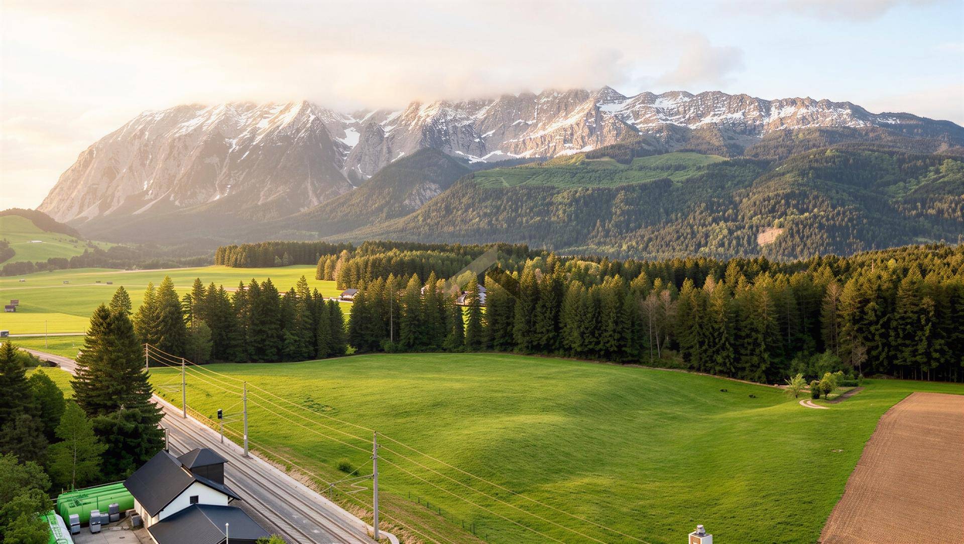 Weitläufige Landschaft mit grünen Feldern, Wäldern und schneebedeckten Bergen im Hintergrund.