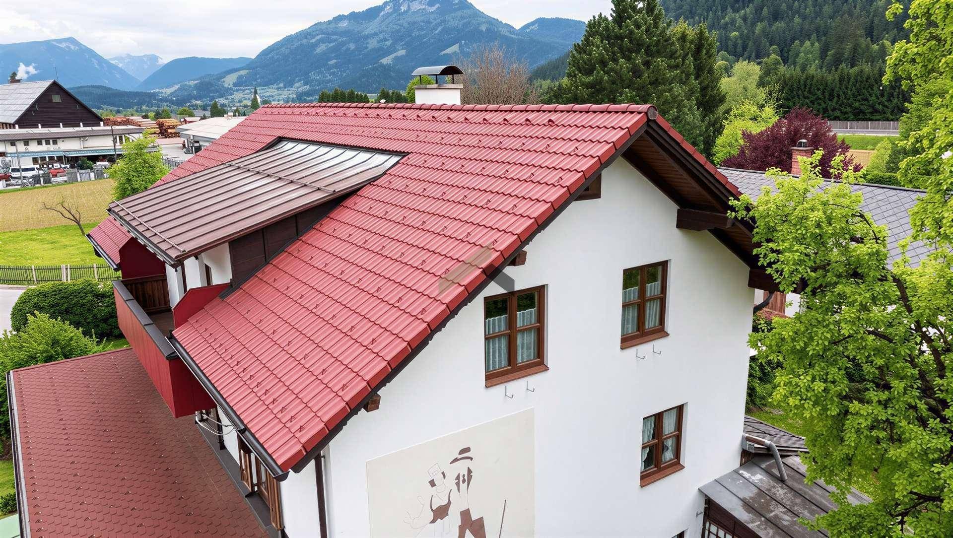 Seitenansicht des Hauses mit rotem Ziegeldach, Balkon und malerischer Berglandschaft im Hintergrund.