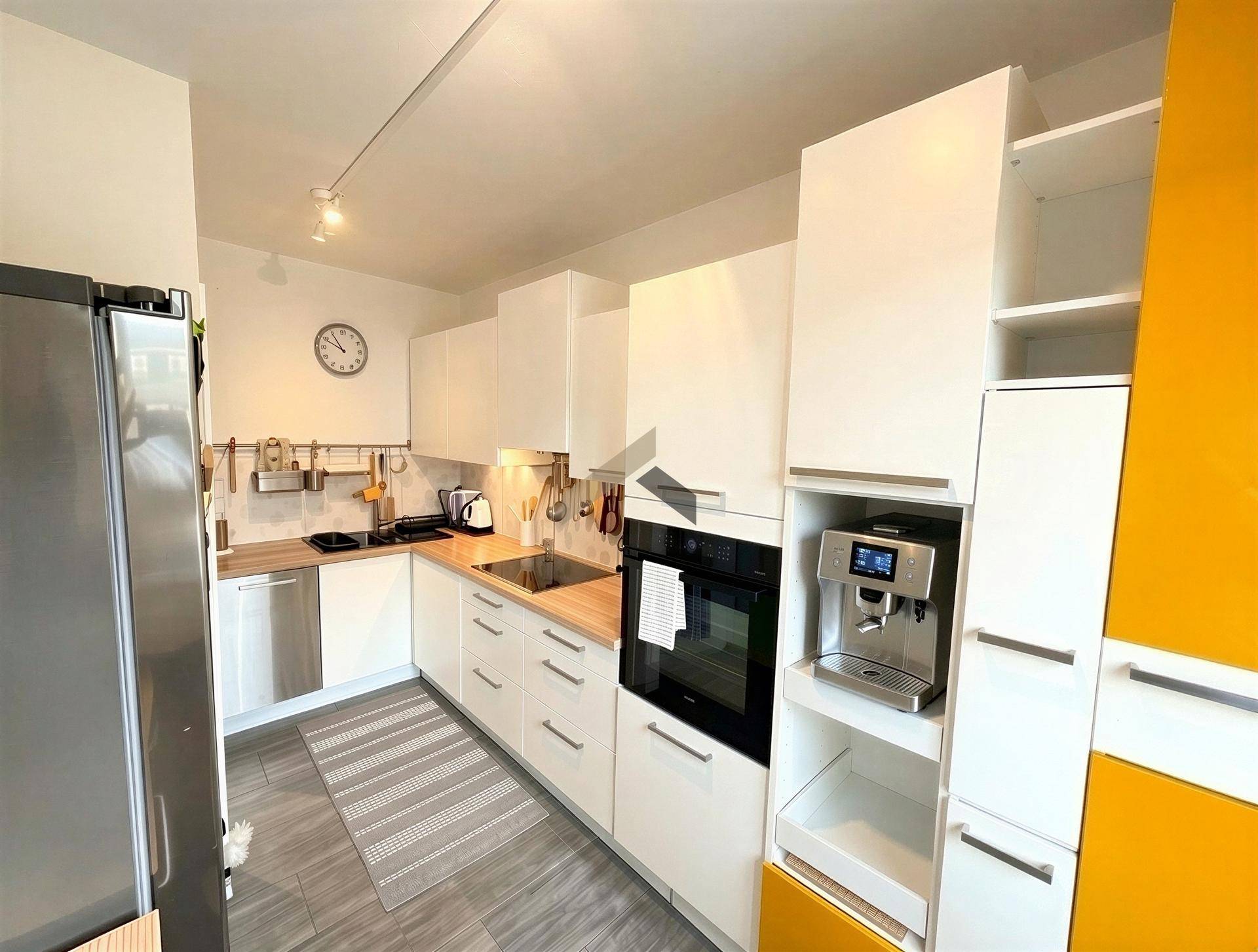 Moderne Einbauküche mit weißen und gelben Fronten, ausgestattet mit hochwertigen Geräten und Fliesenboden.