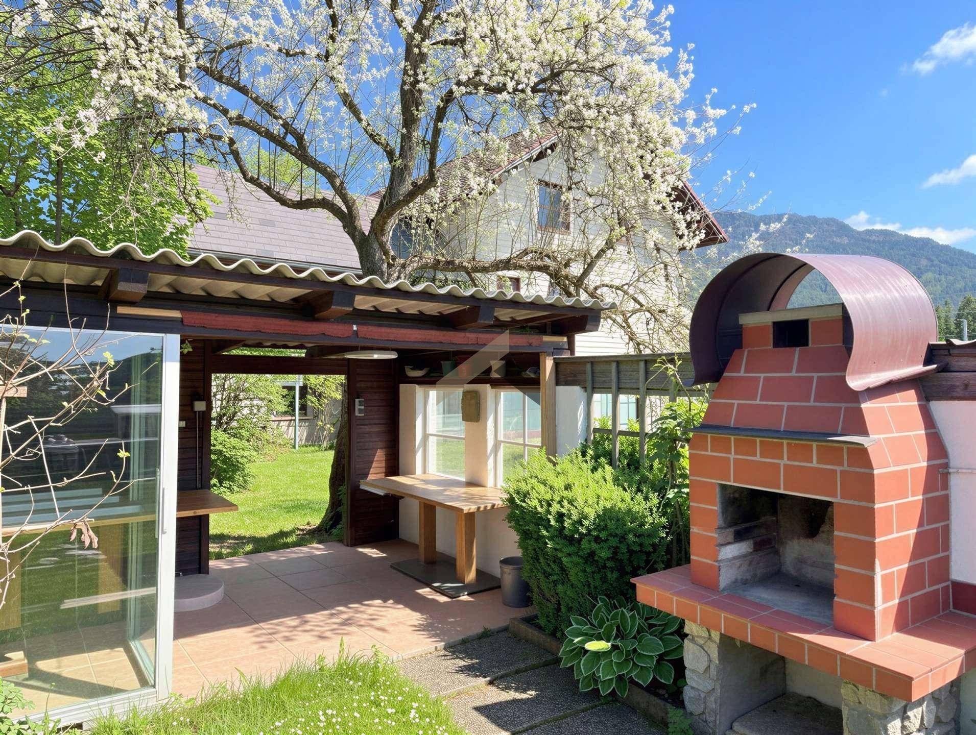Gemütlicher Grillplatz im Garten mit überdachtem Sitzbereich und blühendem Baum.