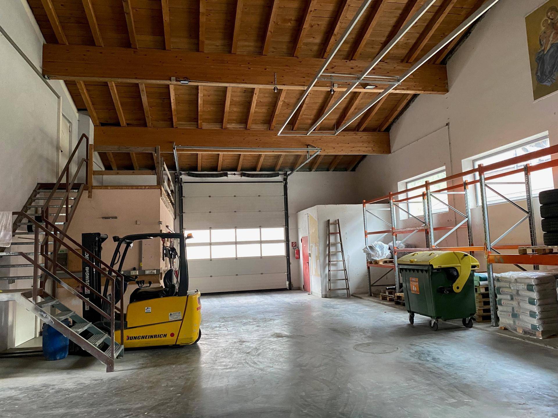 Geräumige Lagerhalle mit hohen Decken, sichtbaren Holzbalken und einem großen Rolltor für den Zugang.