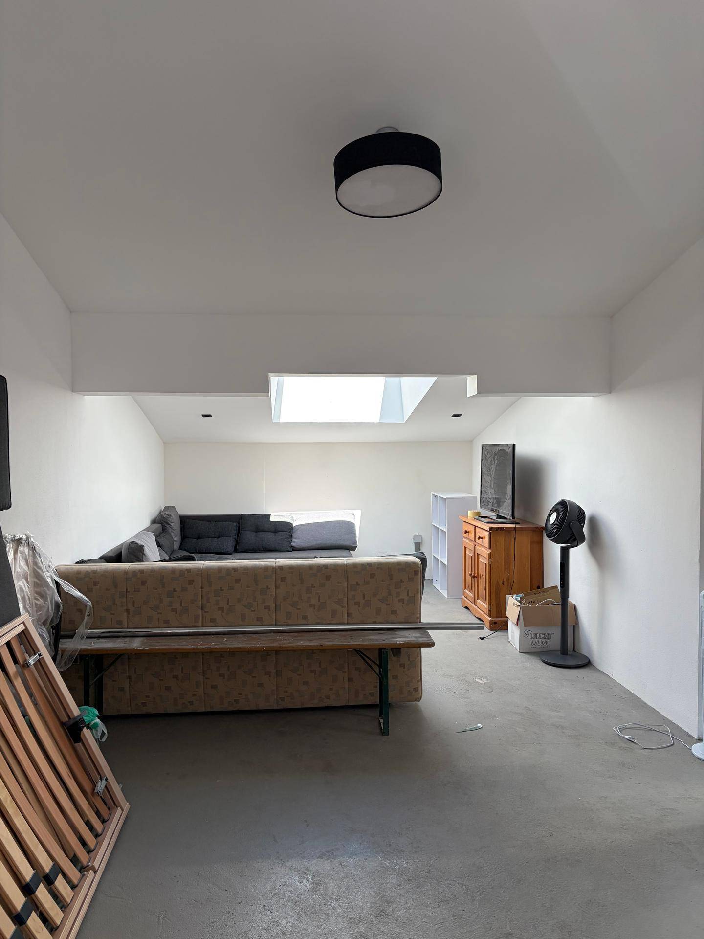 Geräumiger Wohnbereich mit Betonboden, Sofa und einem Dachfenster, das den Raum erhellt.