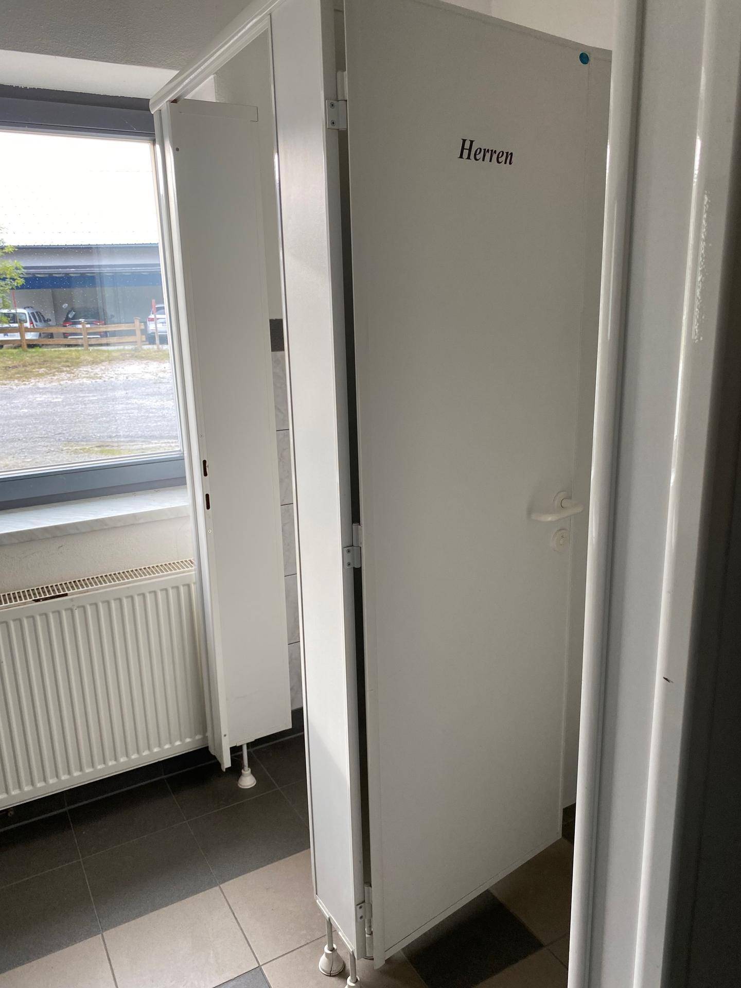 Herrentoilette mit Kabinen und einem Fenster, das für Belüftung und natürliches Licht sorgt.