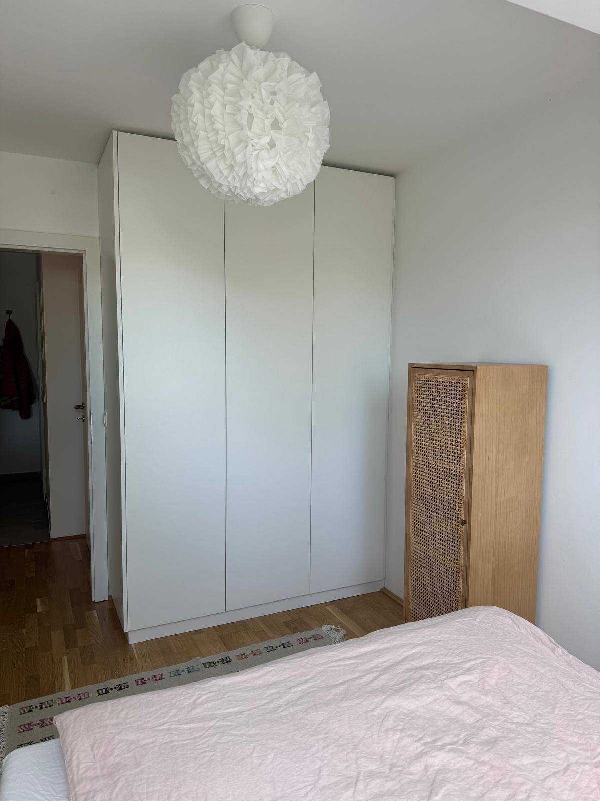 Schlafzimmer mit weißem Kleiderschrank, Holzboden und moderner Deckenleuchte.