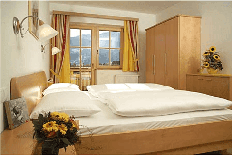 Gemütliches Schlafzimmer mit Doppelbett, Holzmöbeln und malerischem Bergblick aus dem Fenster.