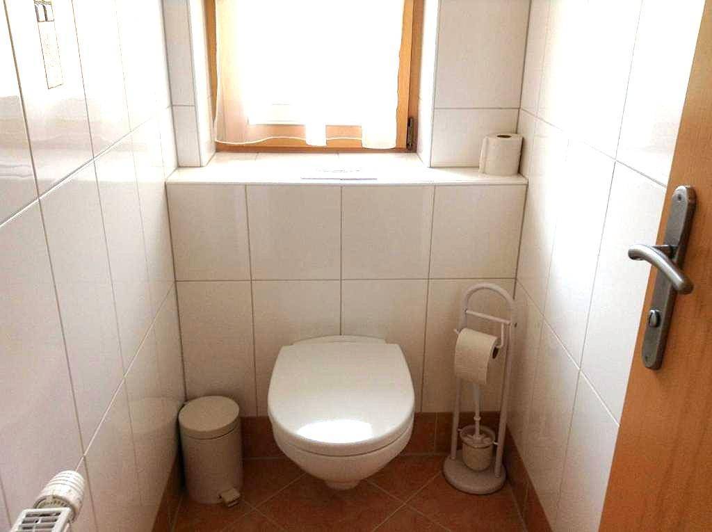 Separates WC mit Toilette, Fenster und hellen Fliesen an Wänden und Boden.