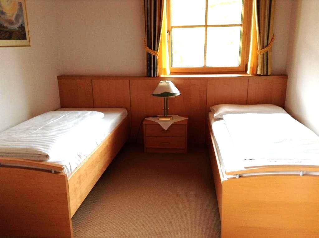 Schlafzimmer mit zwei Einzelbetten, Nachttisch und Fenster, ausgestattet mit Teppichboden.