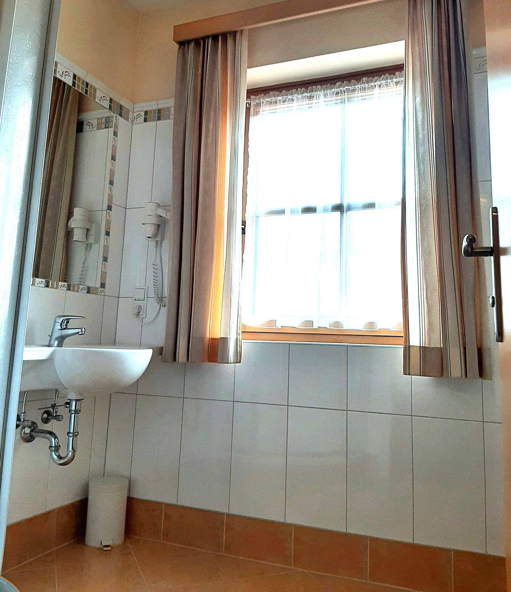 Badezimmer mit Waschbecken, Spiegel und Fenster, gefliest mit hellen Wand- und Bodenfliesen.