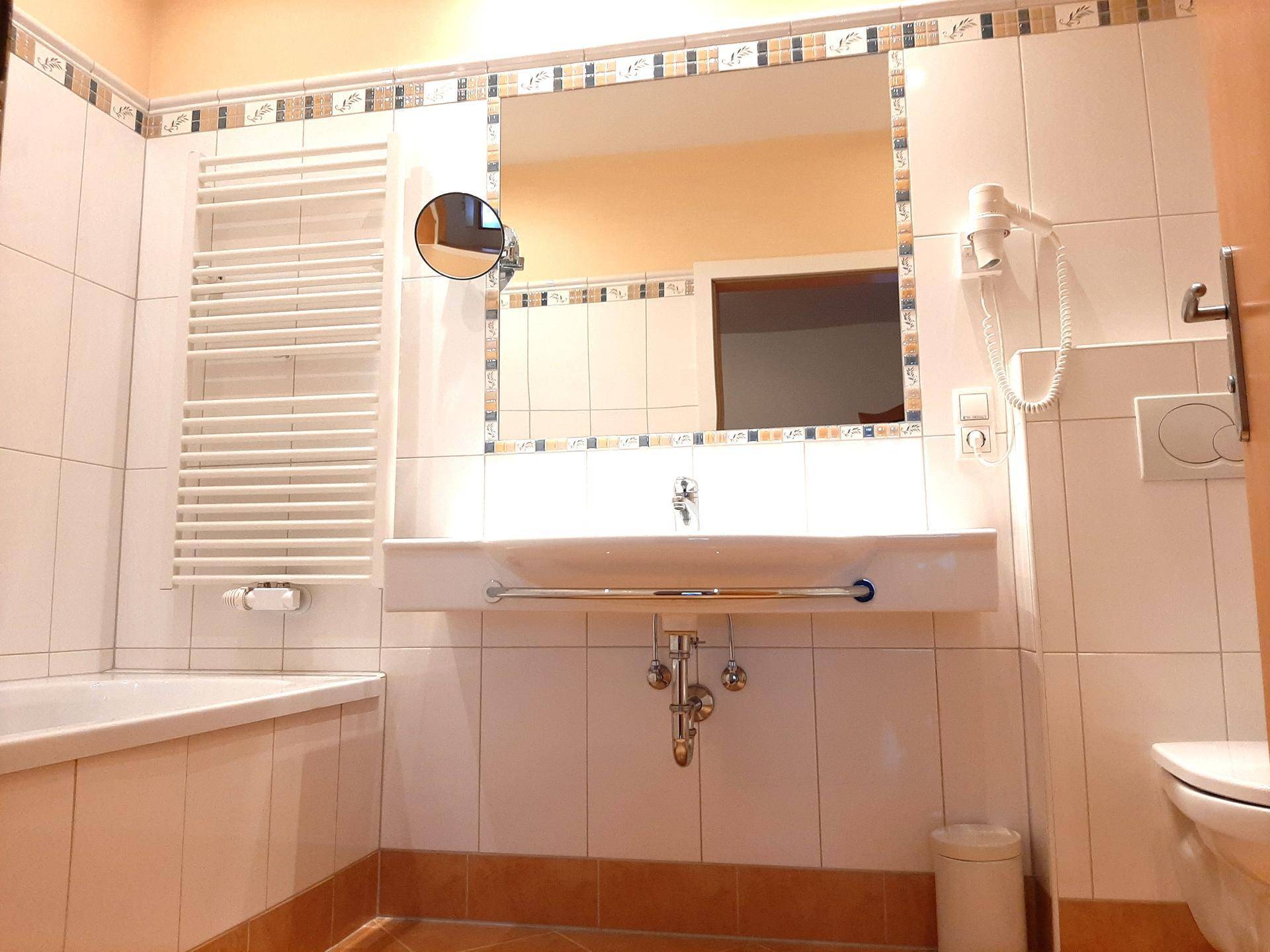 Badezimmer mit Badewanne, Waschbecken, großem Spiegel und beheiztem Handtuchhalter.