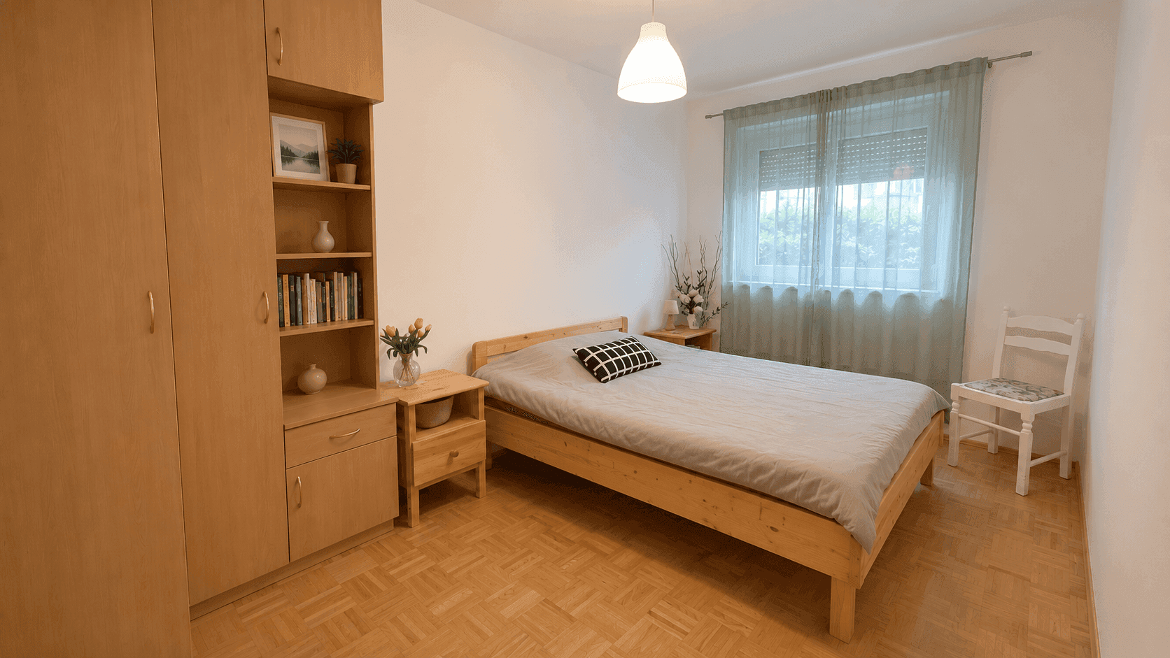 Helles Schlafzimmer mit Holzbett, Kleiderschrank und Parkettboden, gut beleuchtet durch ein Fenster.
