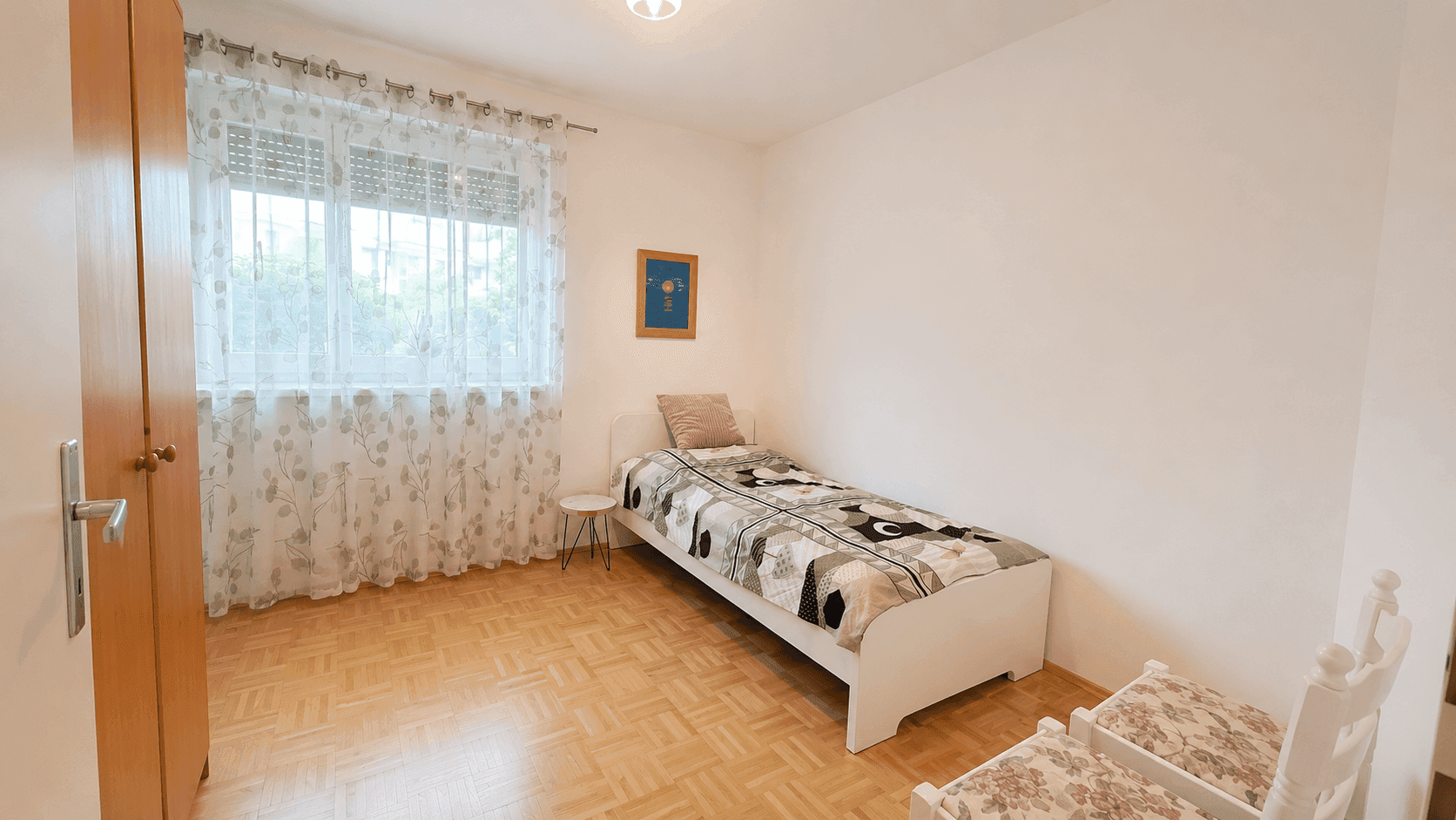 Freundliches Kinderzimmer mit Einzelbett, Parkettboden und großem Fenster für viel Tageslicht.